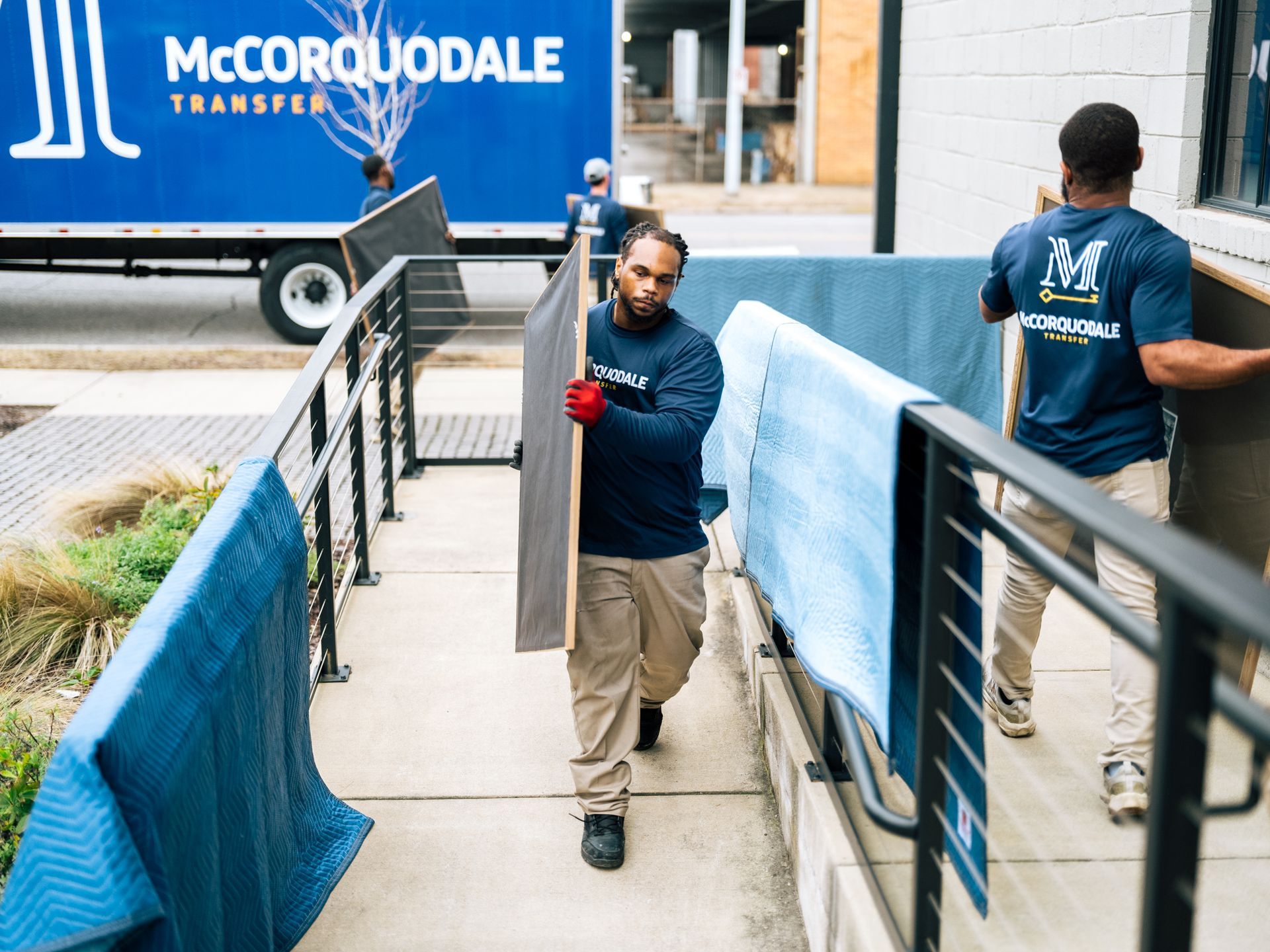 Movers from McCorquodale Transfer carrying items out of building, covered in blue padding.