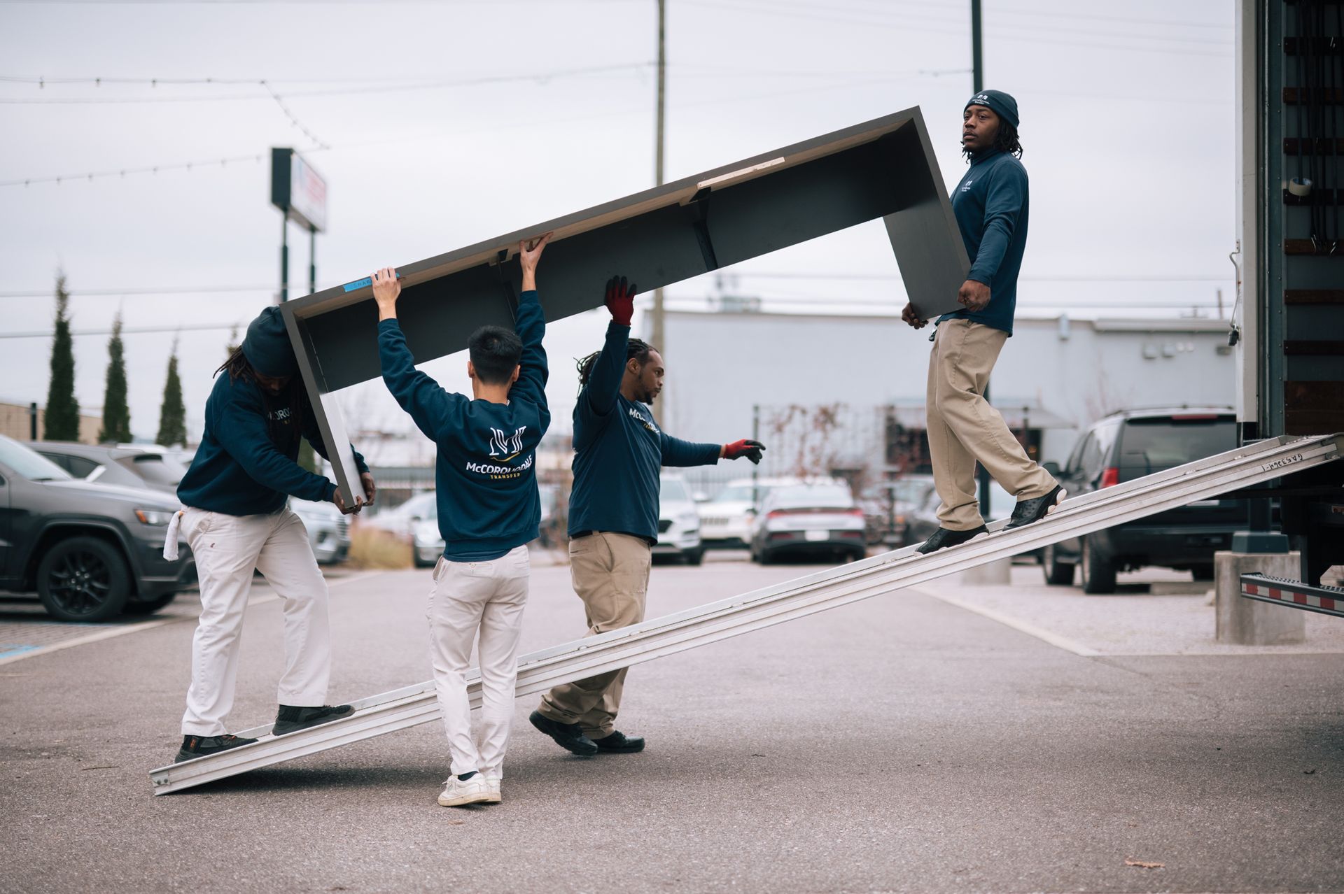 Four people carrying a long metal object up a ramp in a parking lot.