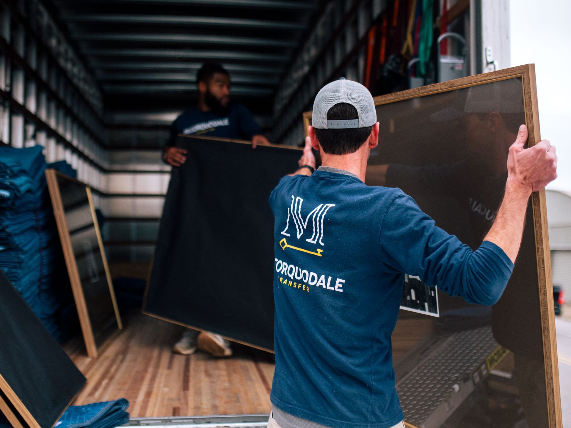 Two movers loading large framed art pieces into a moving truck.