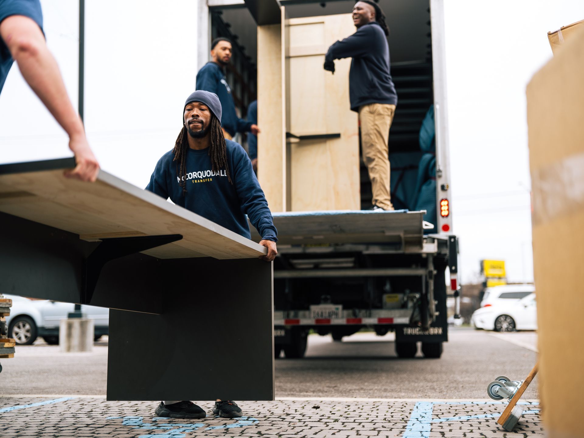 Movers loading furniture into a truck: desk being carried outside by two people, others in the background.
