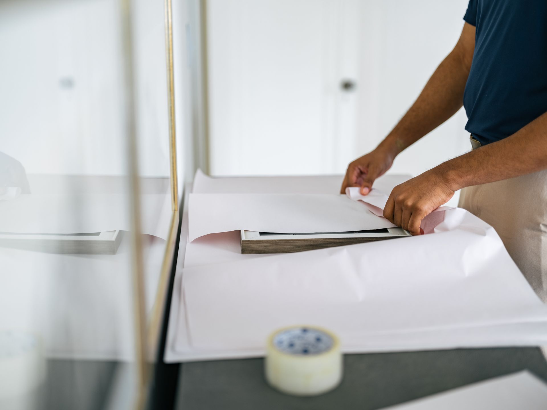 Person wraps papers on a table, preparing a package. Tape roll visible.