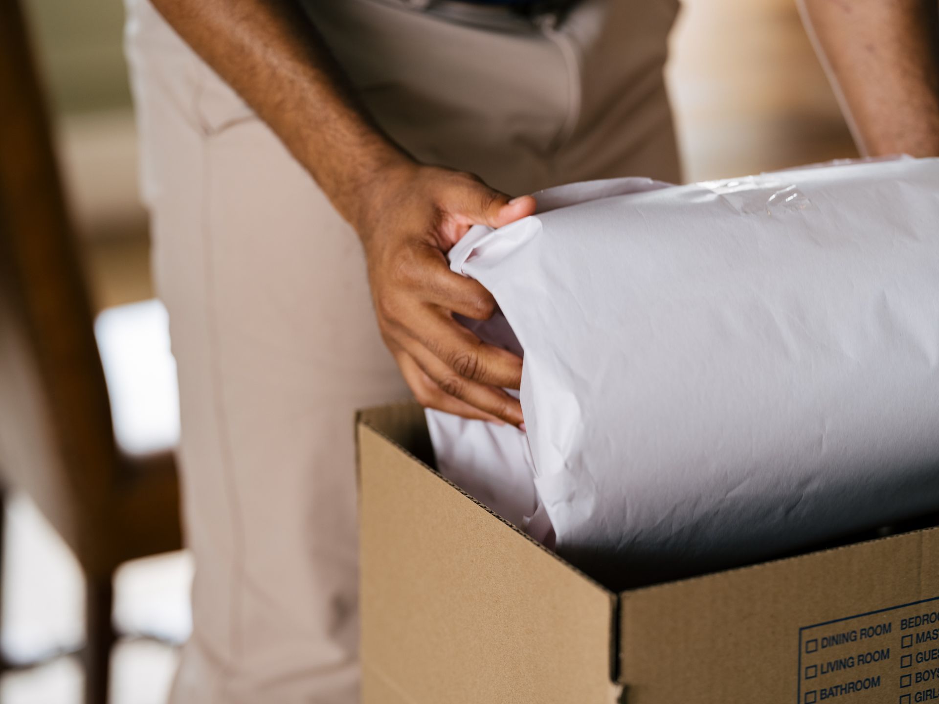 Person packing a wrapped item into a cardboard box indoors.