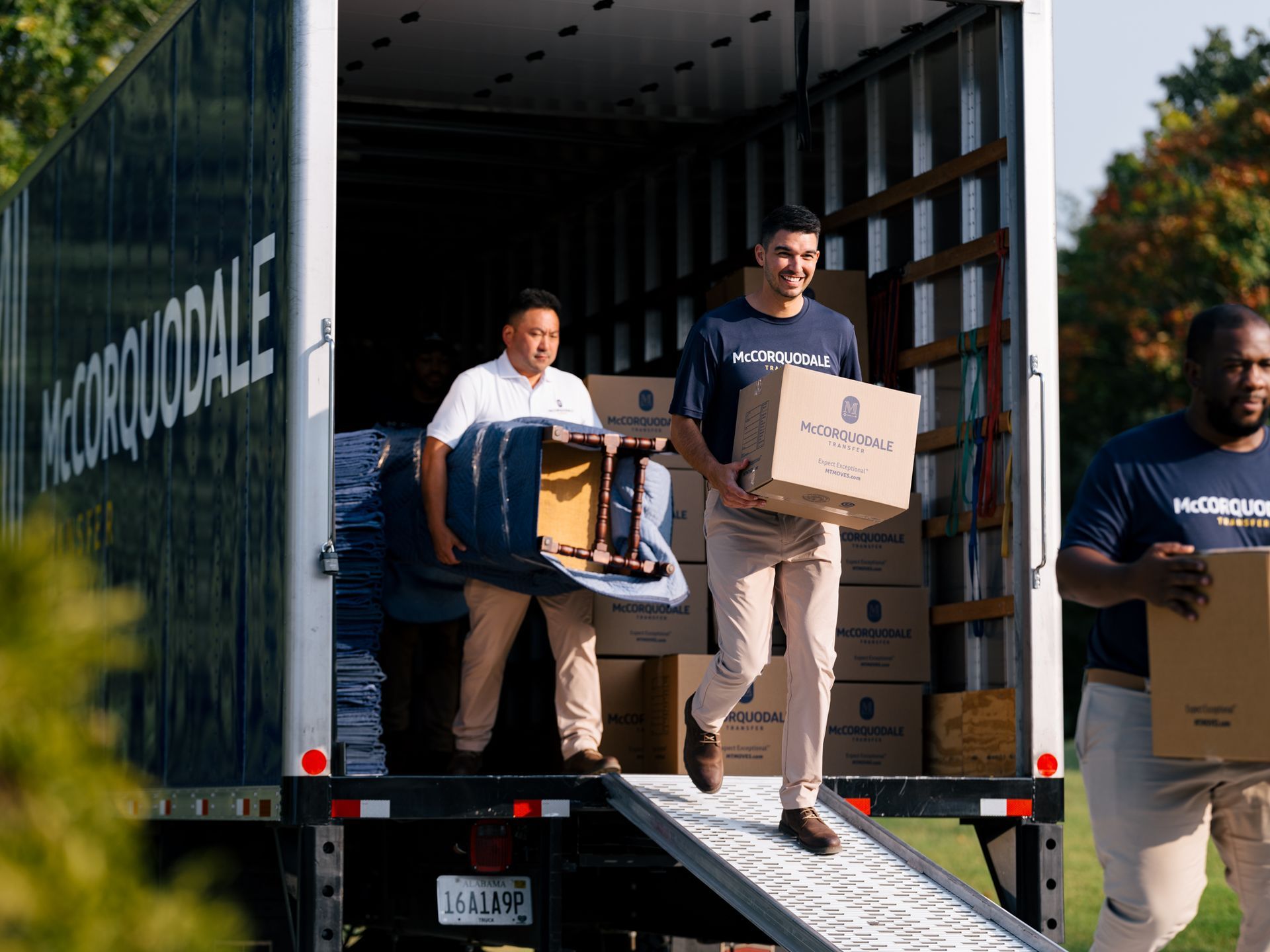 Movers unloading a truck, carrying boxes and furniture. Outdoors, sunny day.