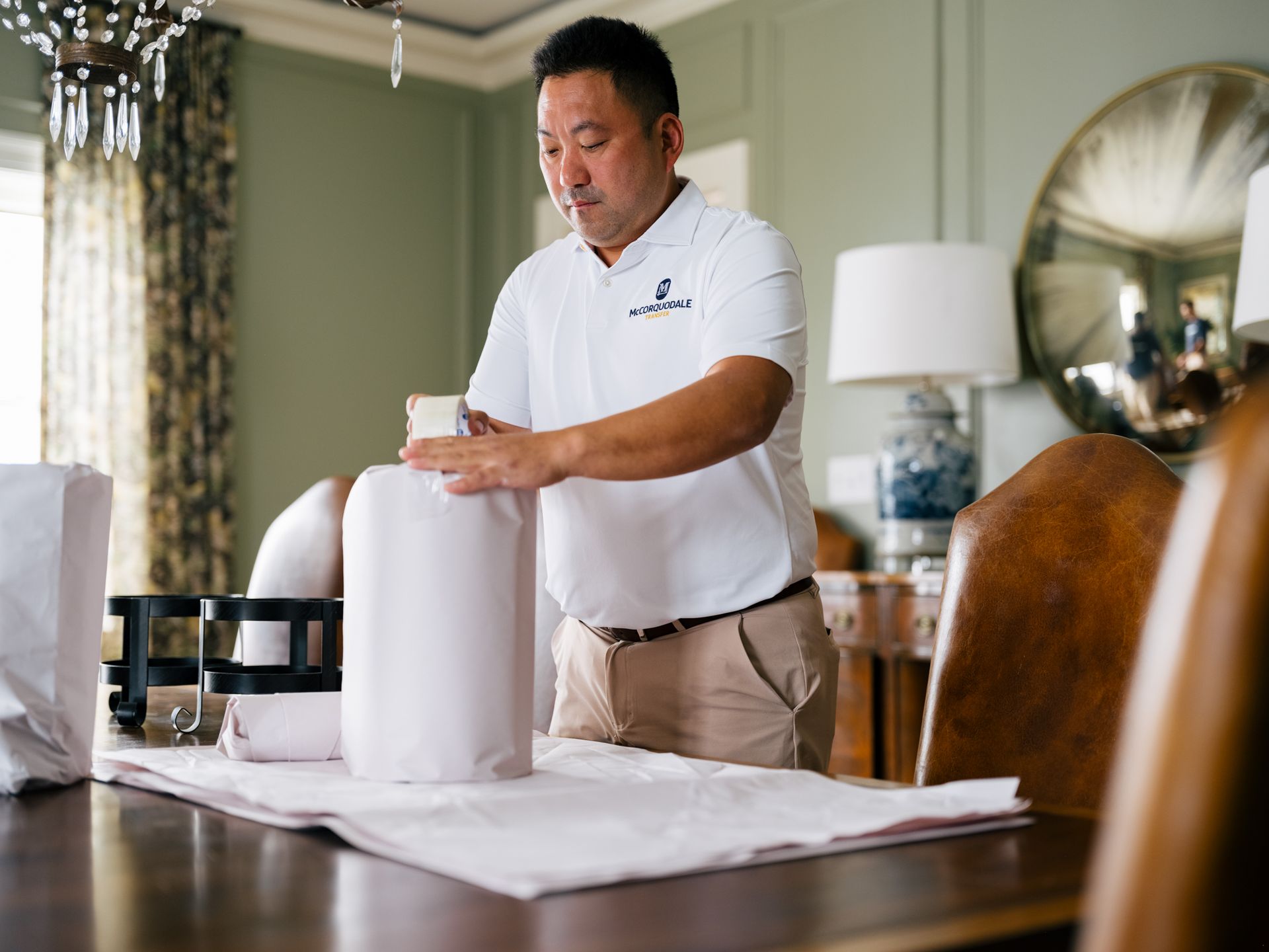 Man in polo shirt packing items on a table, possibly for delivery in a dining room.