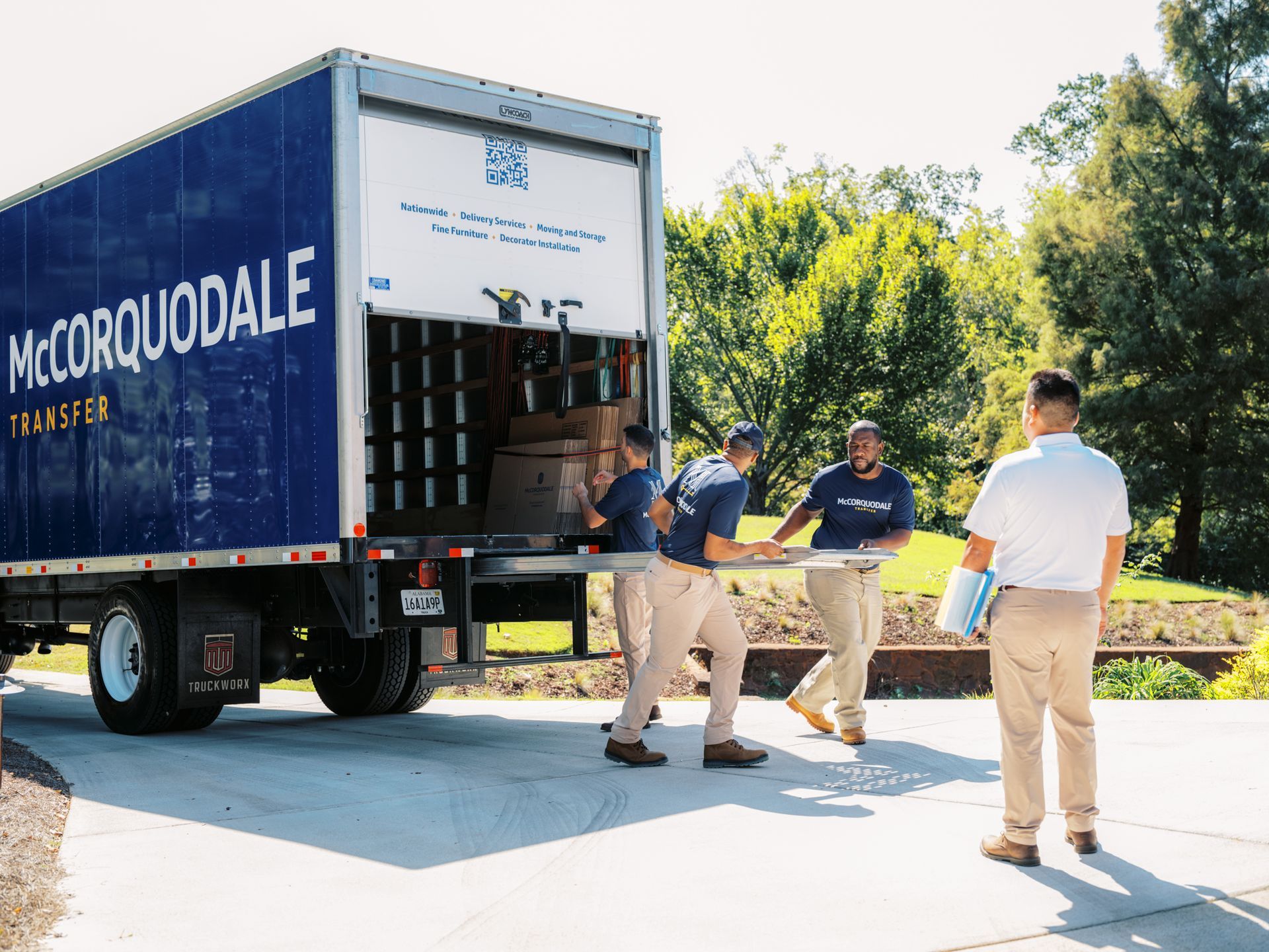 Movers loading a McCorquodale Transfer truck with boxes and furniture in a driveway.