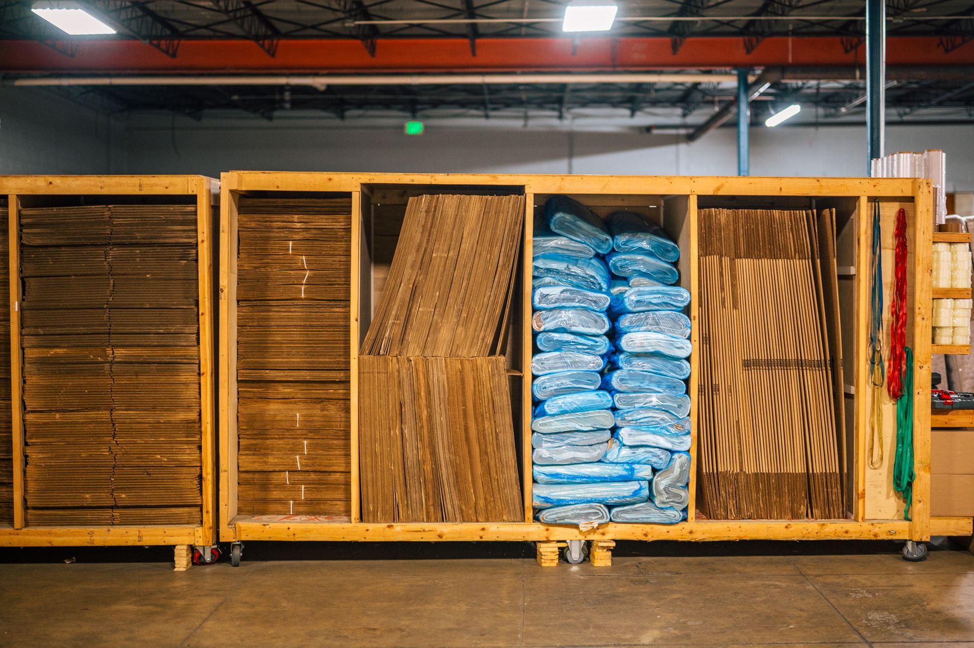 Wooden shelving unit filled with cardboard sheets and blue-wrapped packages inside a warehouse.