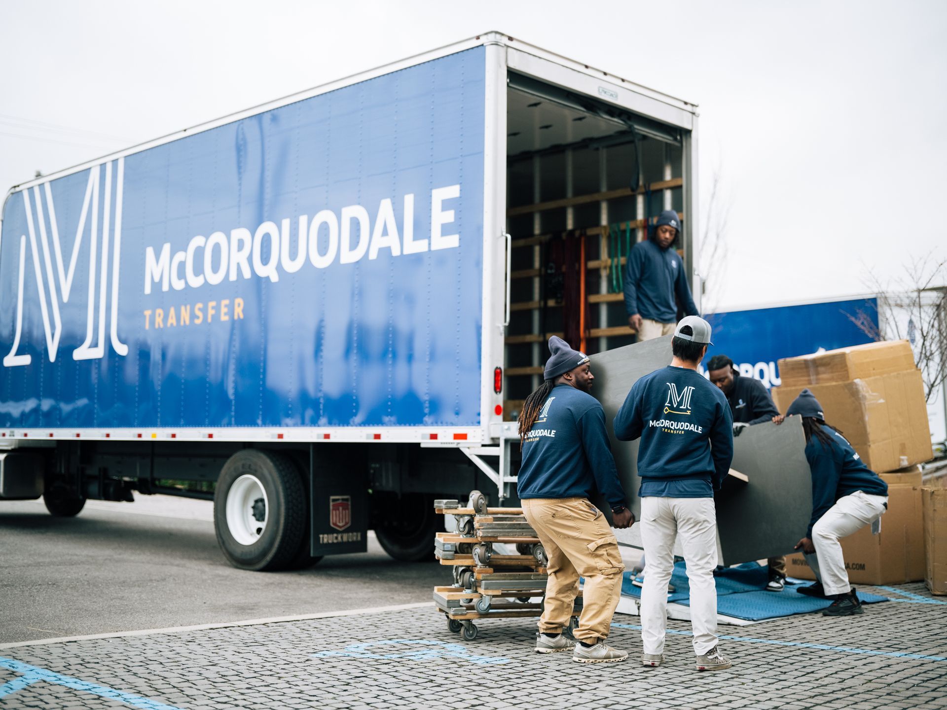 Movers loading furniture into a blue McCorquodale Transfer truck on a cloudy day.