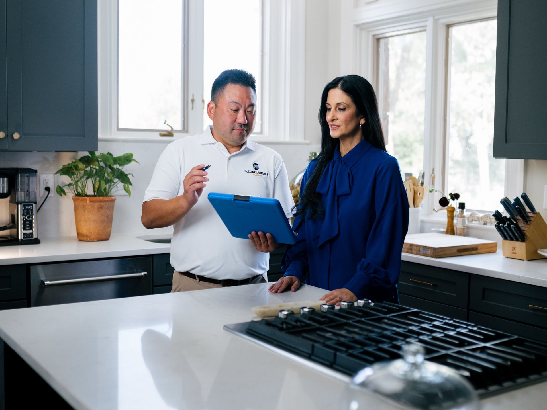 Man in white shirt and woman in blue top reviewing tablet in a kitchen.