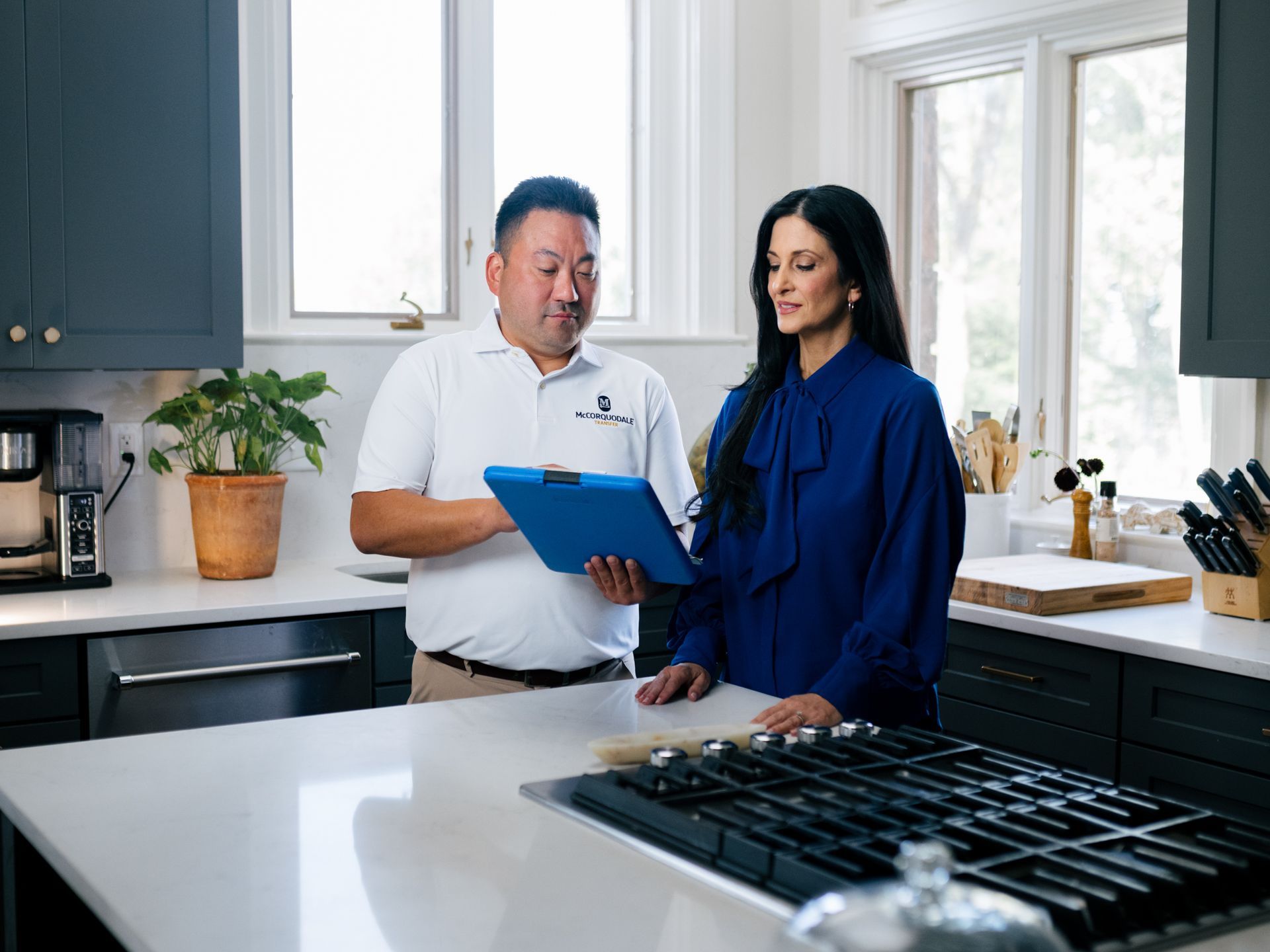 A person in a white uniform and a person in blue attire discuss documents in a kitchen.