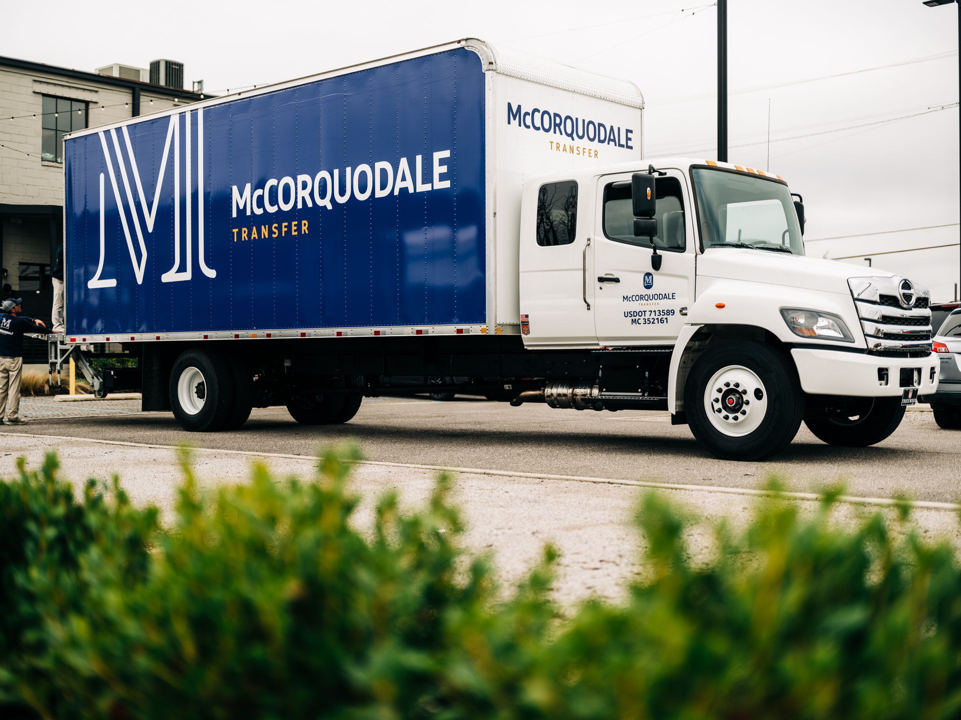 White McCorquodale box truck parked on a gray surface with green bushes in the foreground.