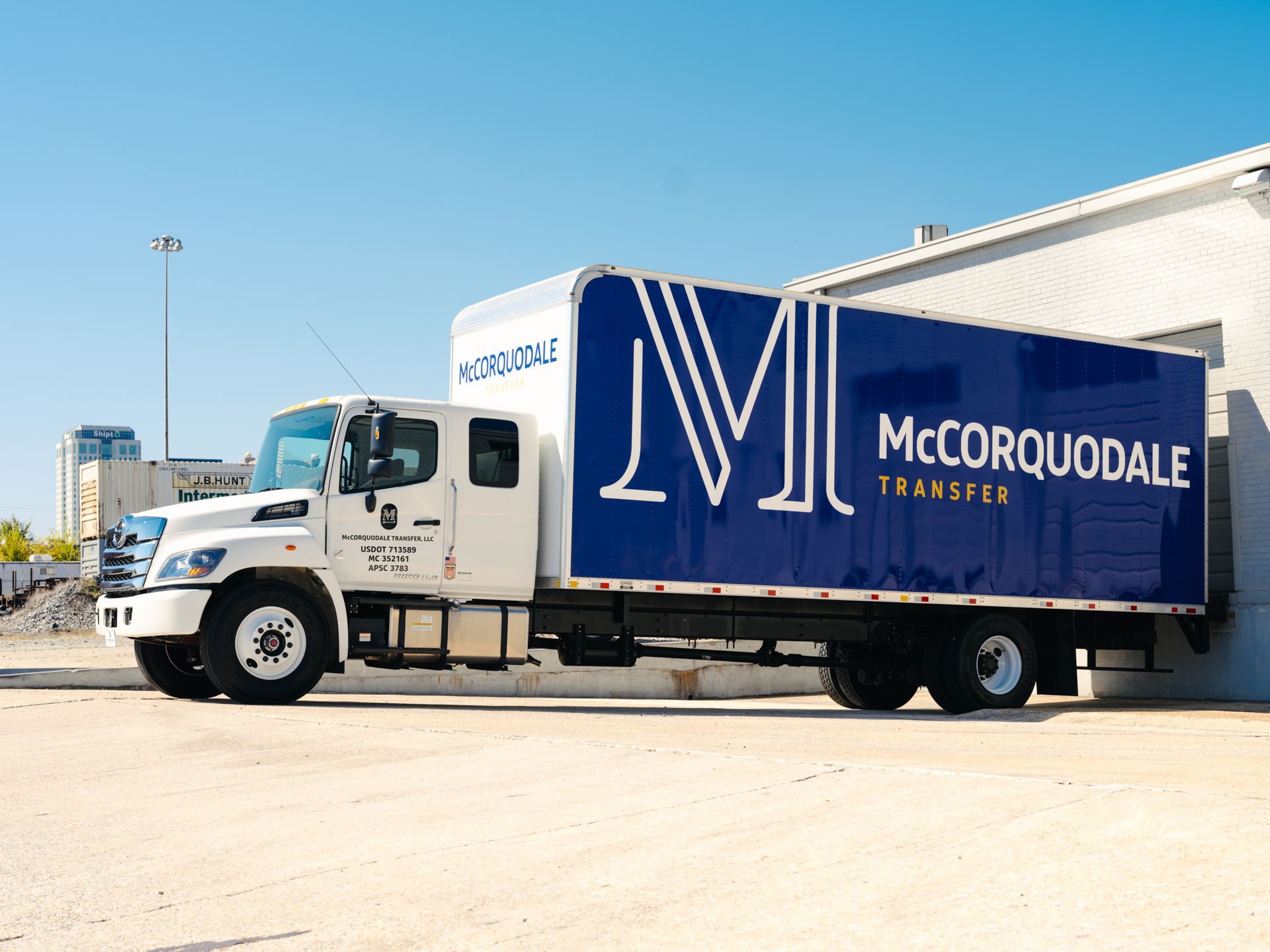 White and blue McCorquodale Transfer truck at a loading dock with a bright blue sky.