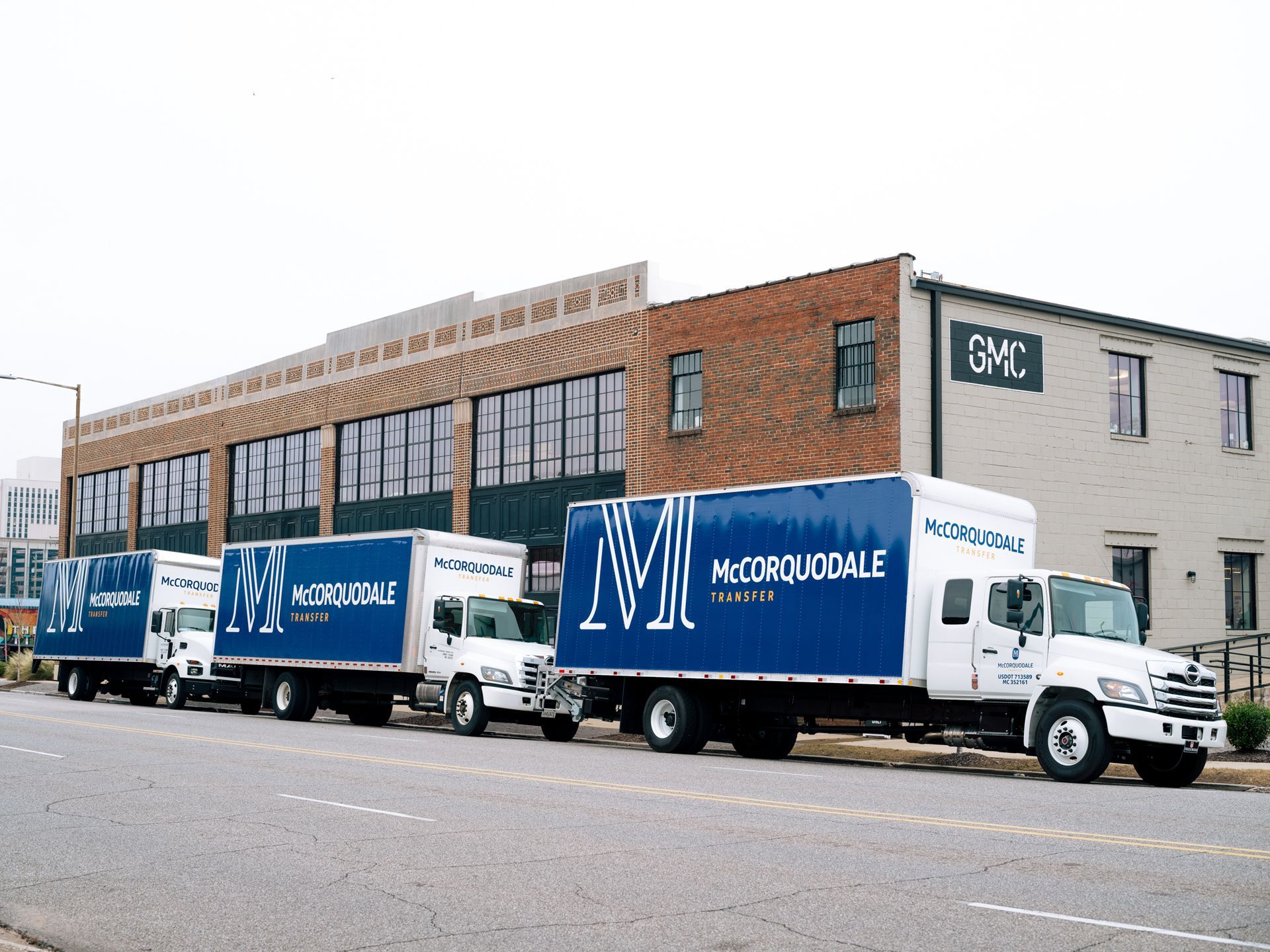 Four moving trucks parked in a row on a city street in front of a brick building.