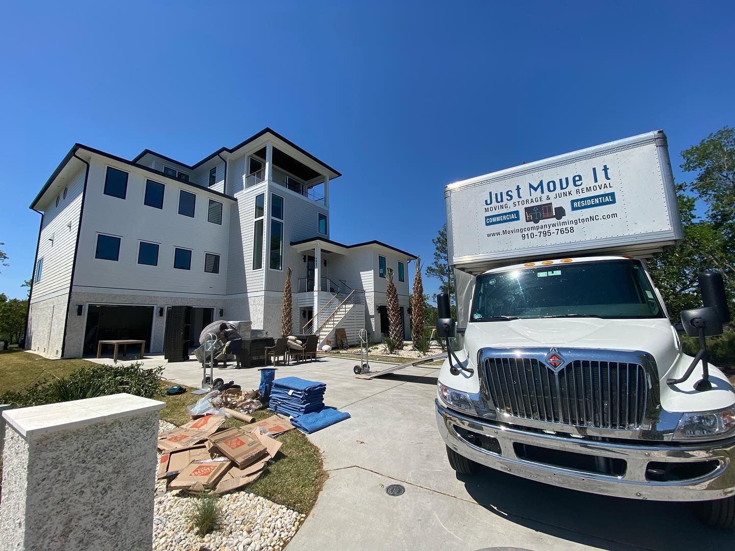 A moving truck is parked in front of a large white house.