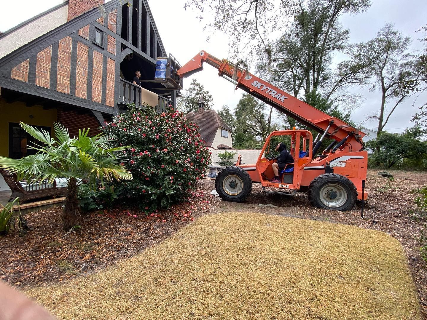 A man is driving a forklift in front of a house.