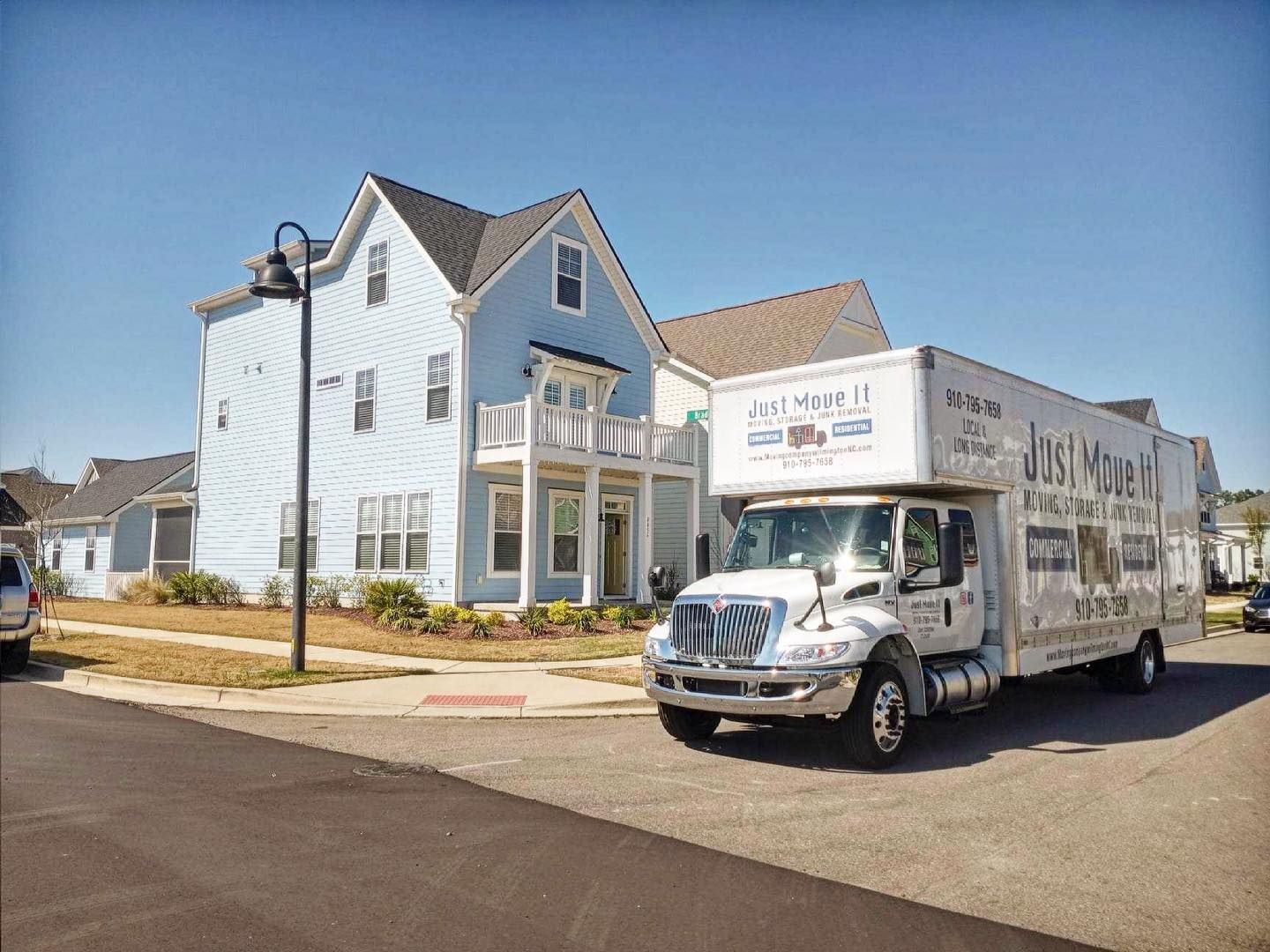 A white moving truck is parked in front of a blue house.