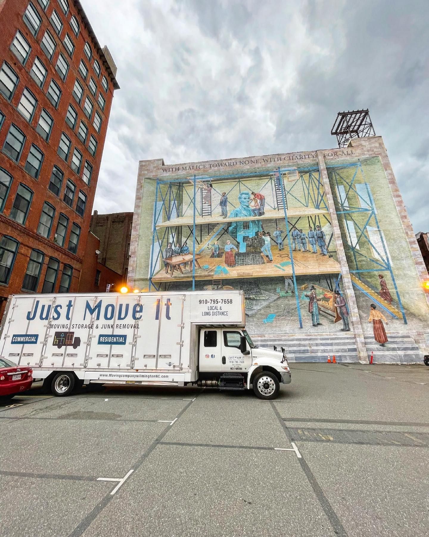 A moving truck is parked in front of a building with a mural on it.