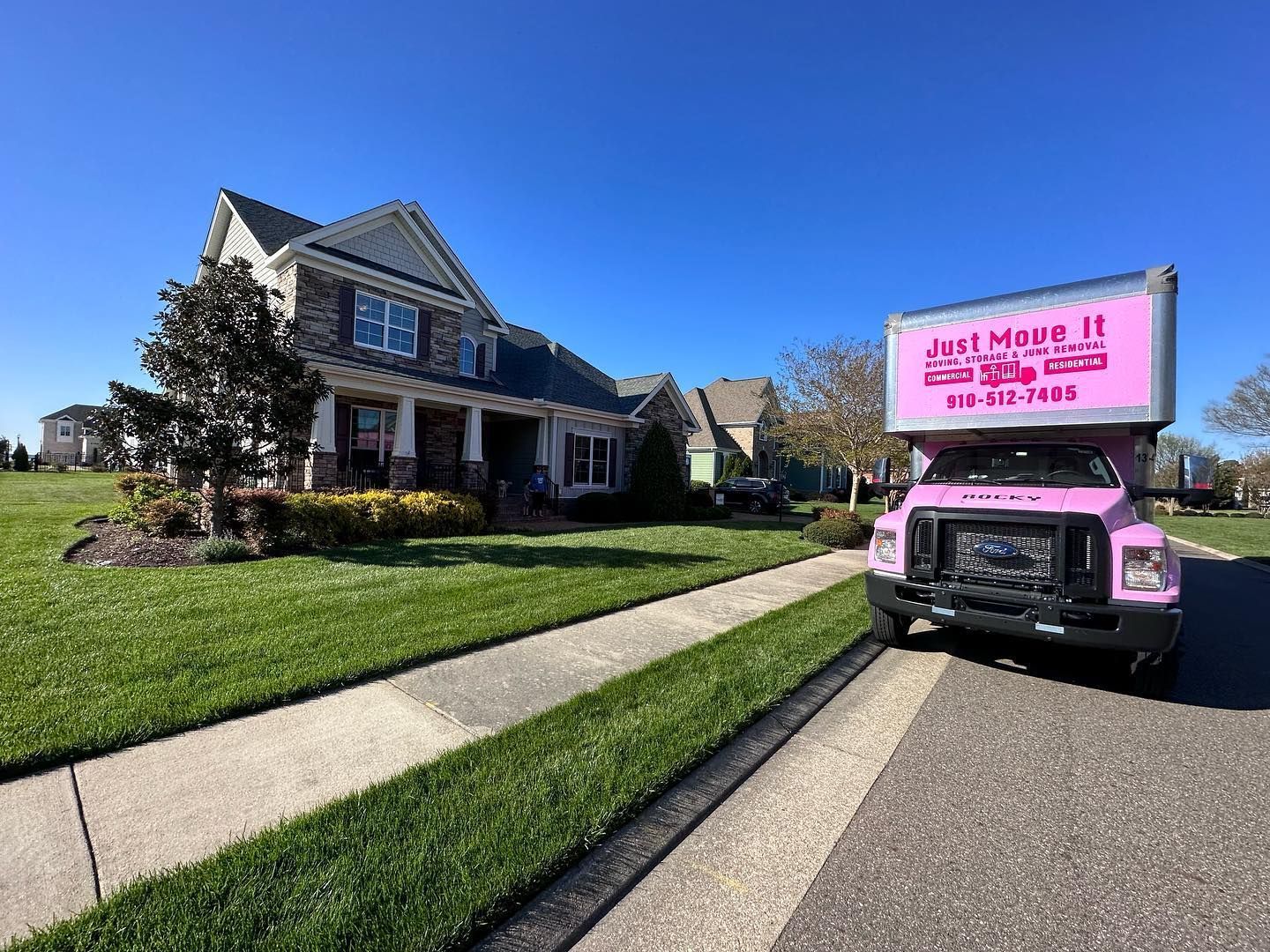 A pink moving truck is parked in front of a house.