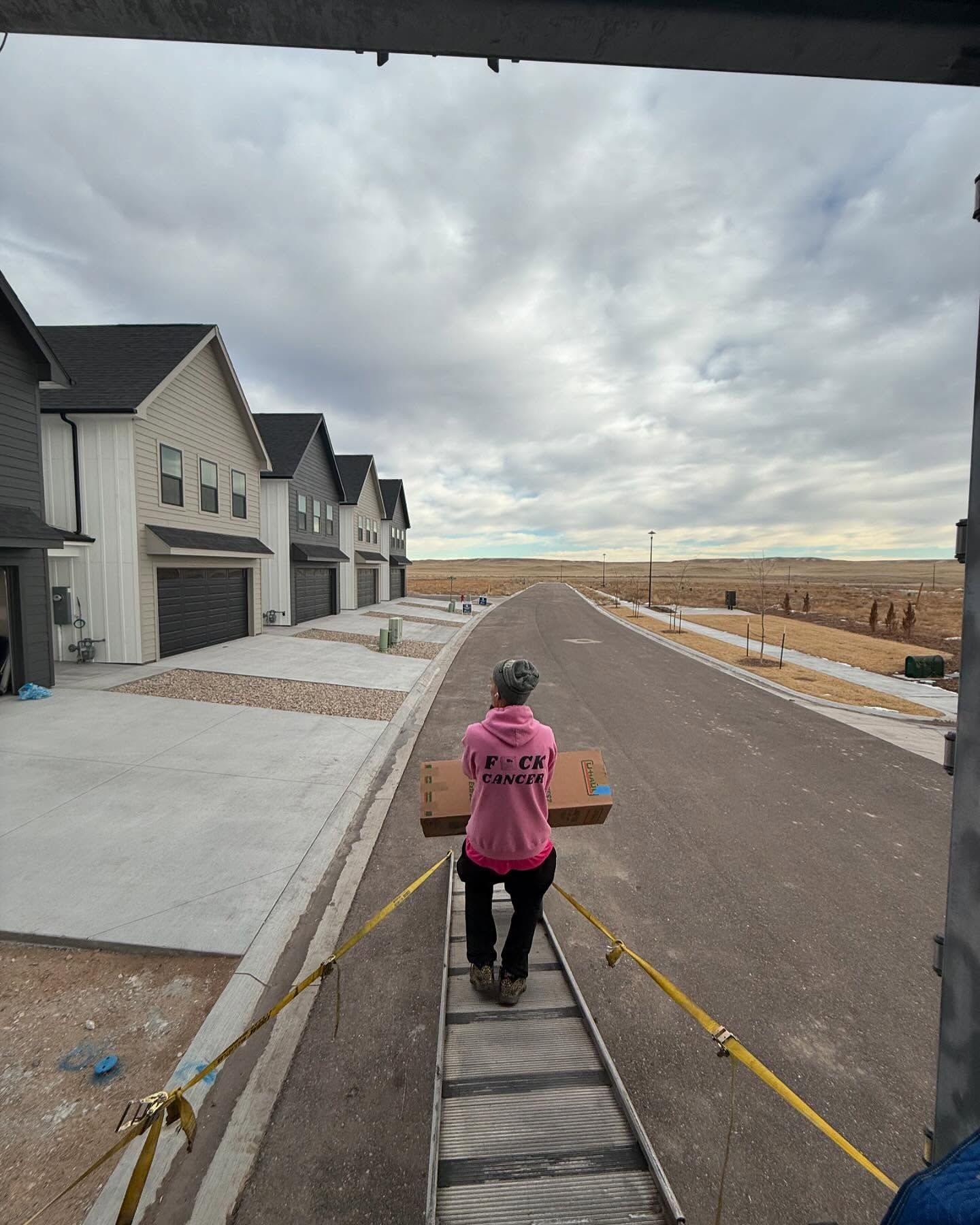 A woman in a pink hoodie is carrying a box down a ladder.