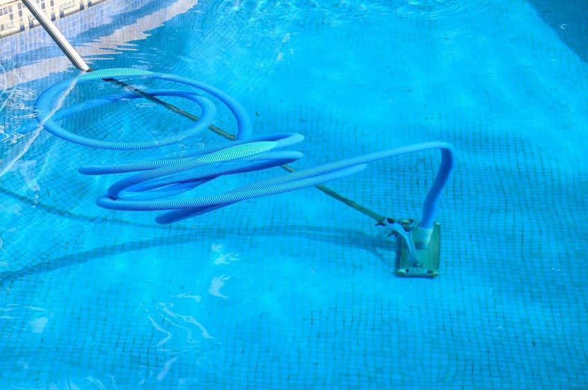 Pool vacuum and hose submerged in a blue-tiled pool. A net is also in the water.