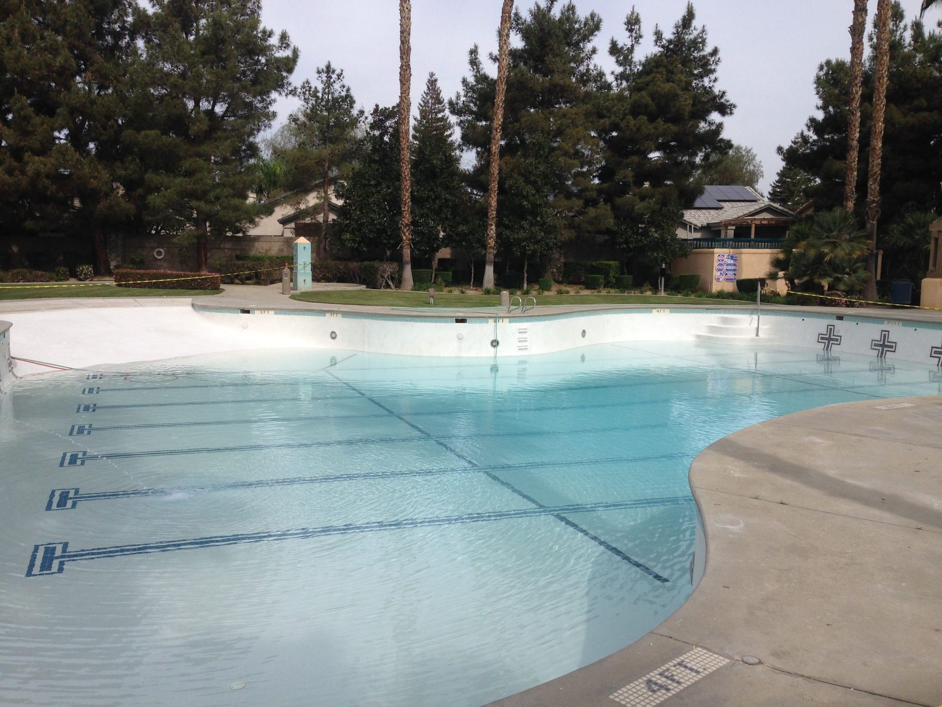 Empty swimming pool with white paint, depth markers, and surrounding trees.
