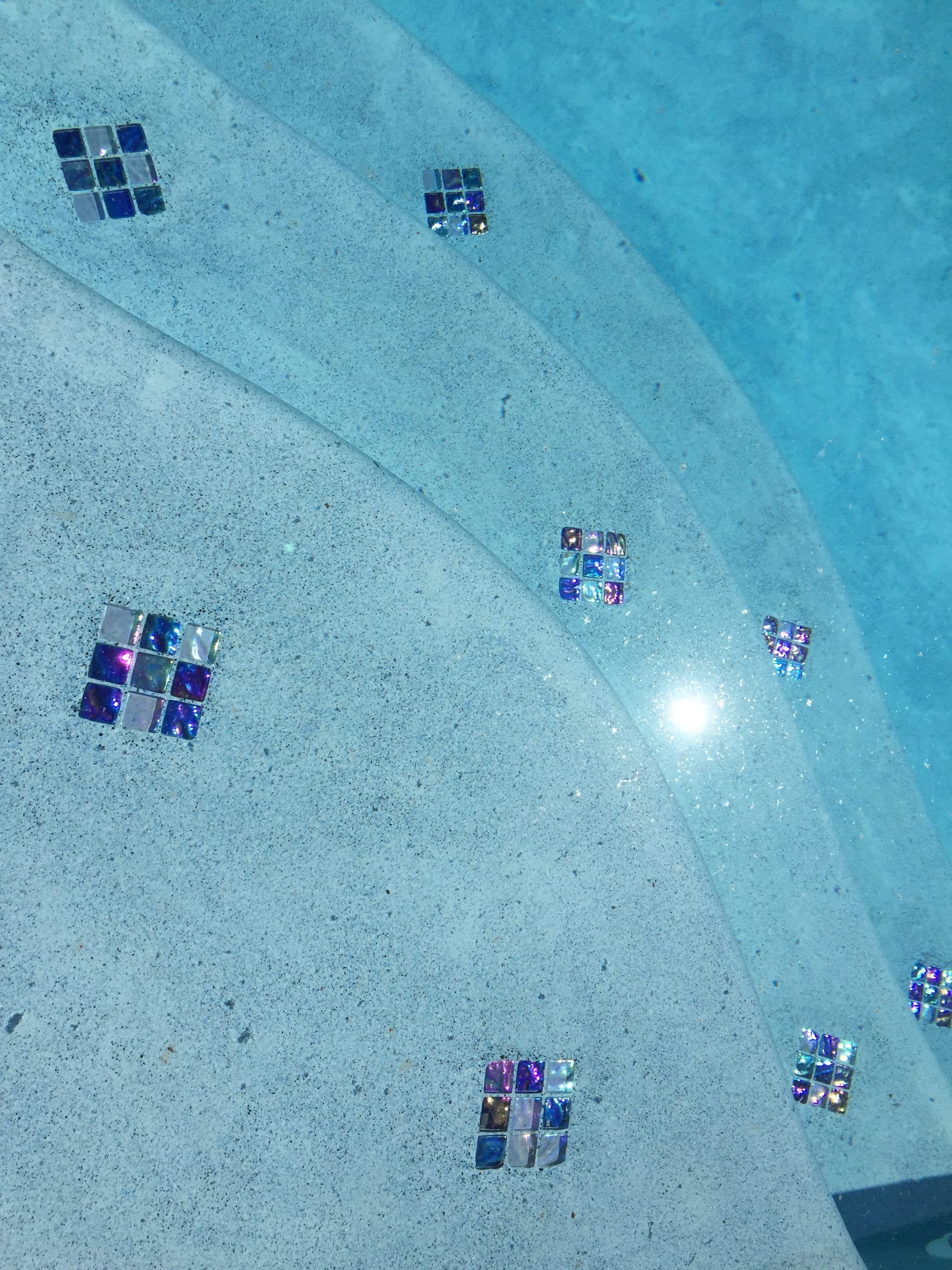 Pool steps with blue water and scattered mosaic tiles.