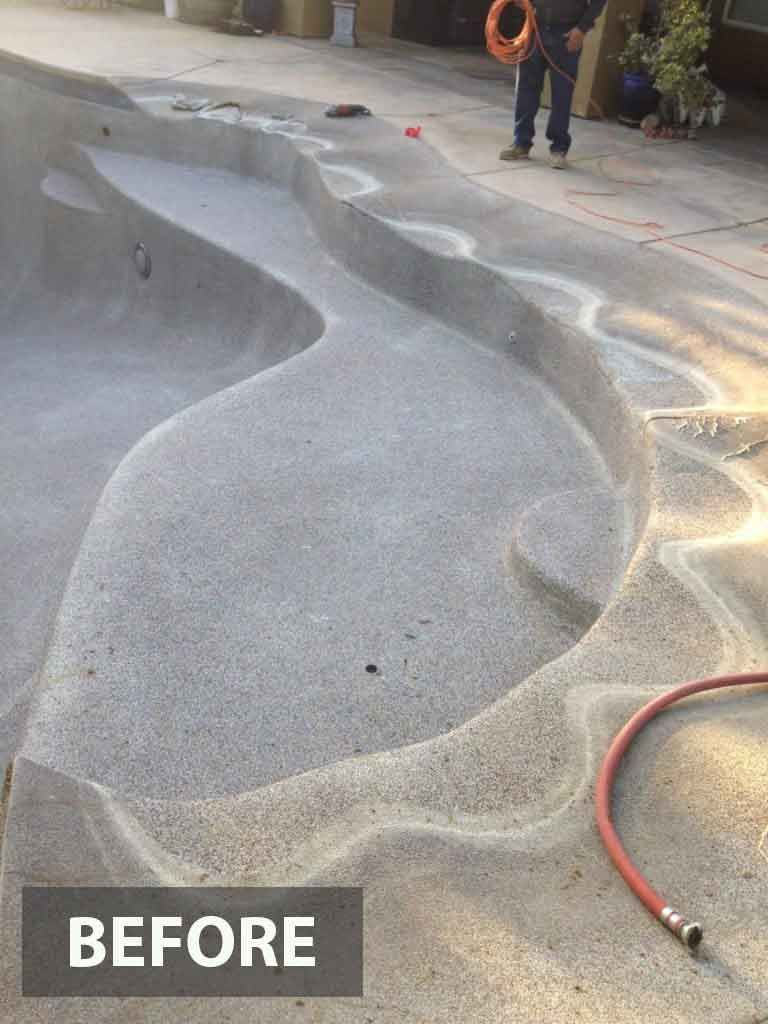 Empty, textured pool with curved edges, being cleaned by a person with a hose.