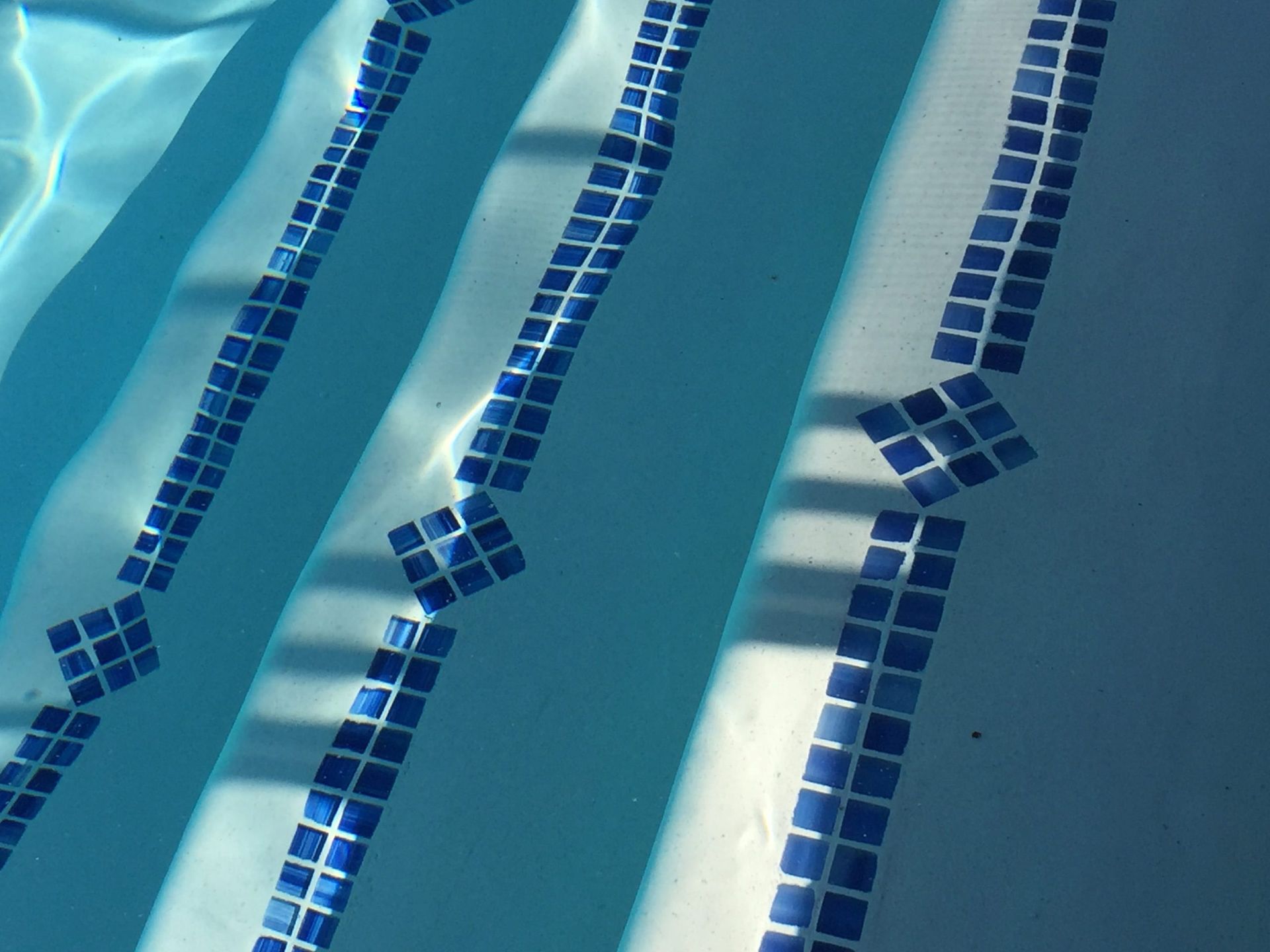 Blue tiled steps in a swimming pool with water rippling on the surface.