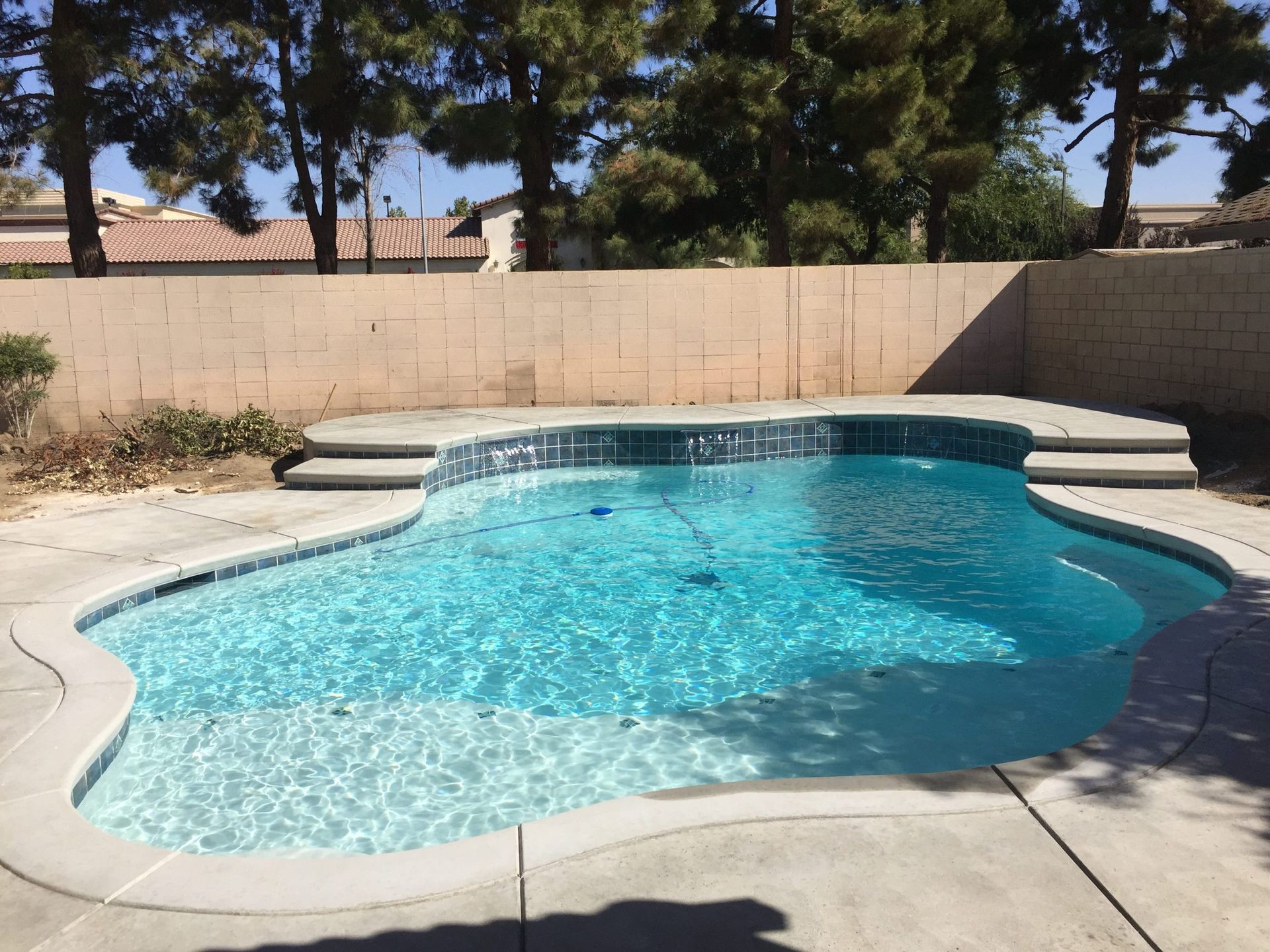 A blue, freeform swimming pool in a backyard with a concrete patio.