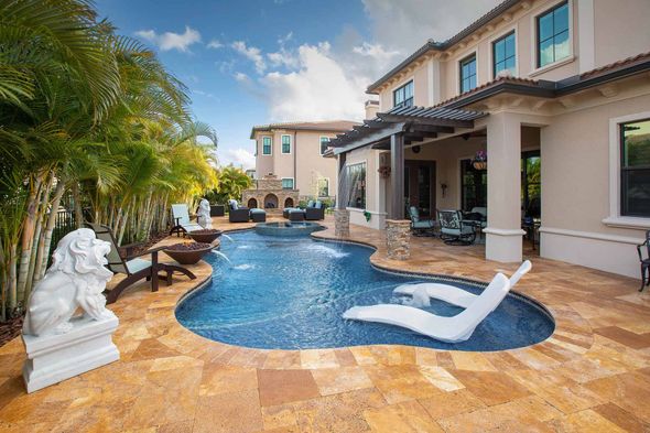 Luxurious backyard with pool and lounge chairs next to a large house, blue water.