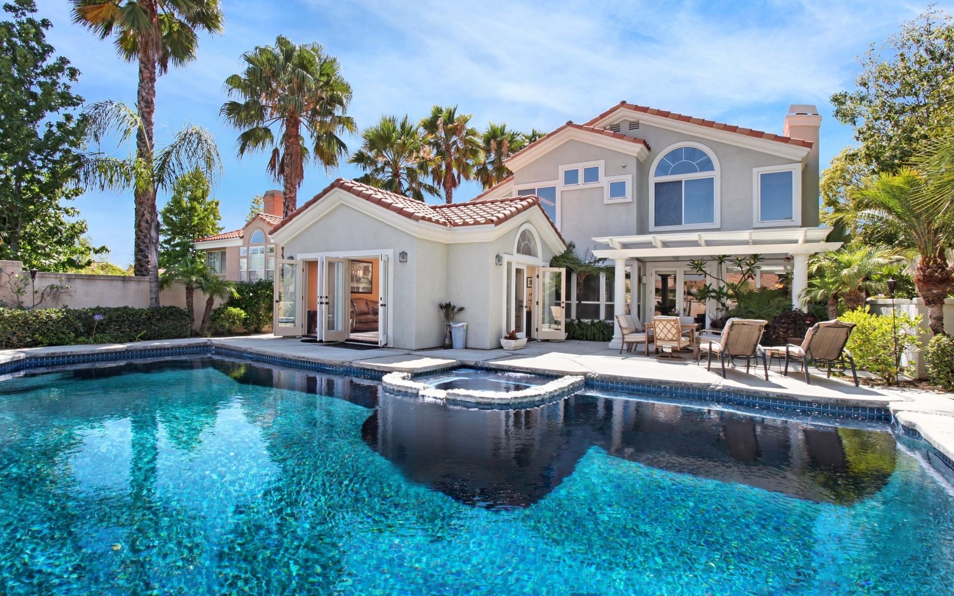A two-story home with a pool, spa, and patio in a sunny setting with palm trees.