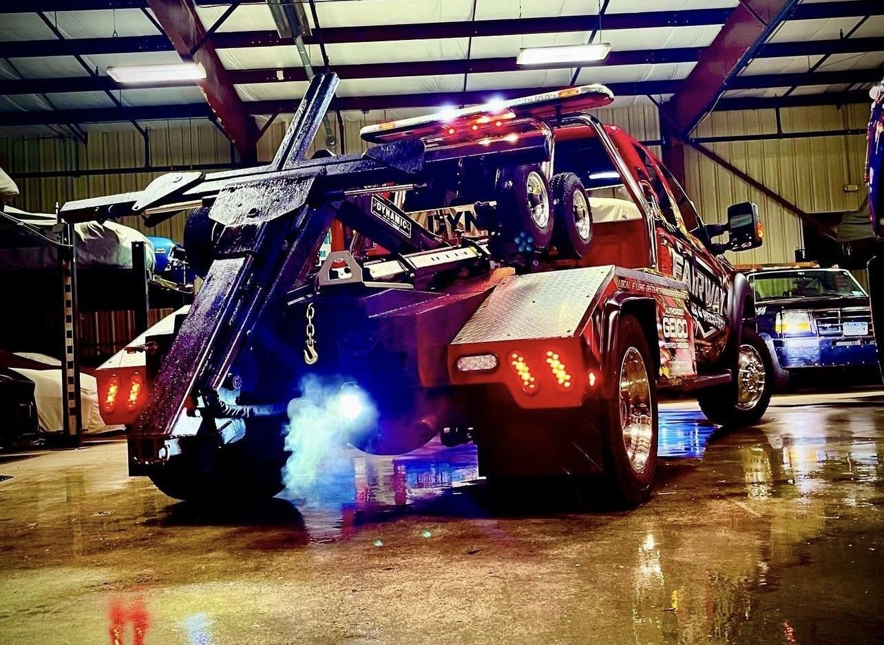 Rear view of a red tow truck with lights flashing, emitting blue exhaust in a garage.