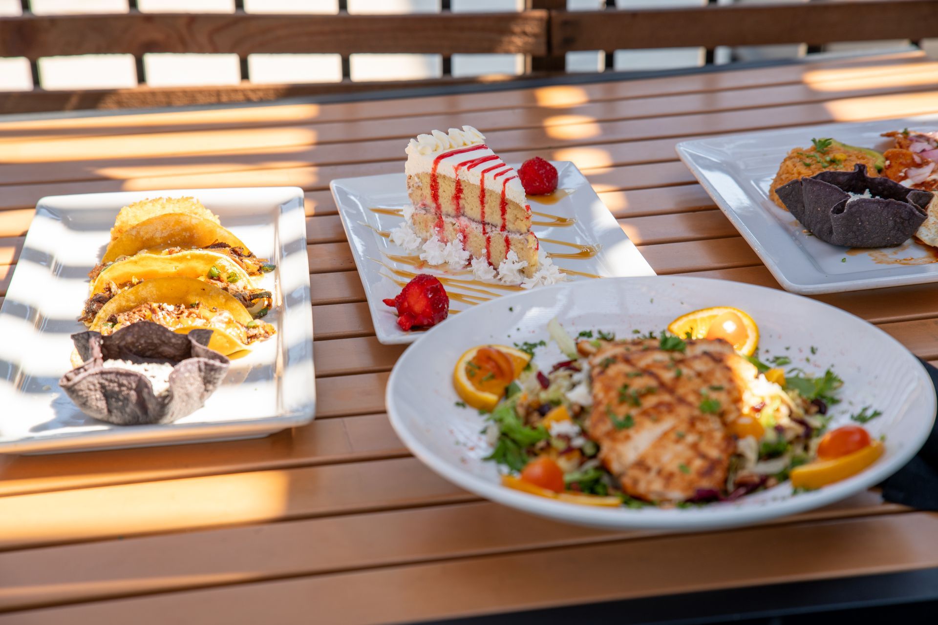 Plates of desserts and a salad on a wooden table, outside with sunlight.