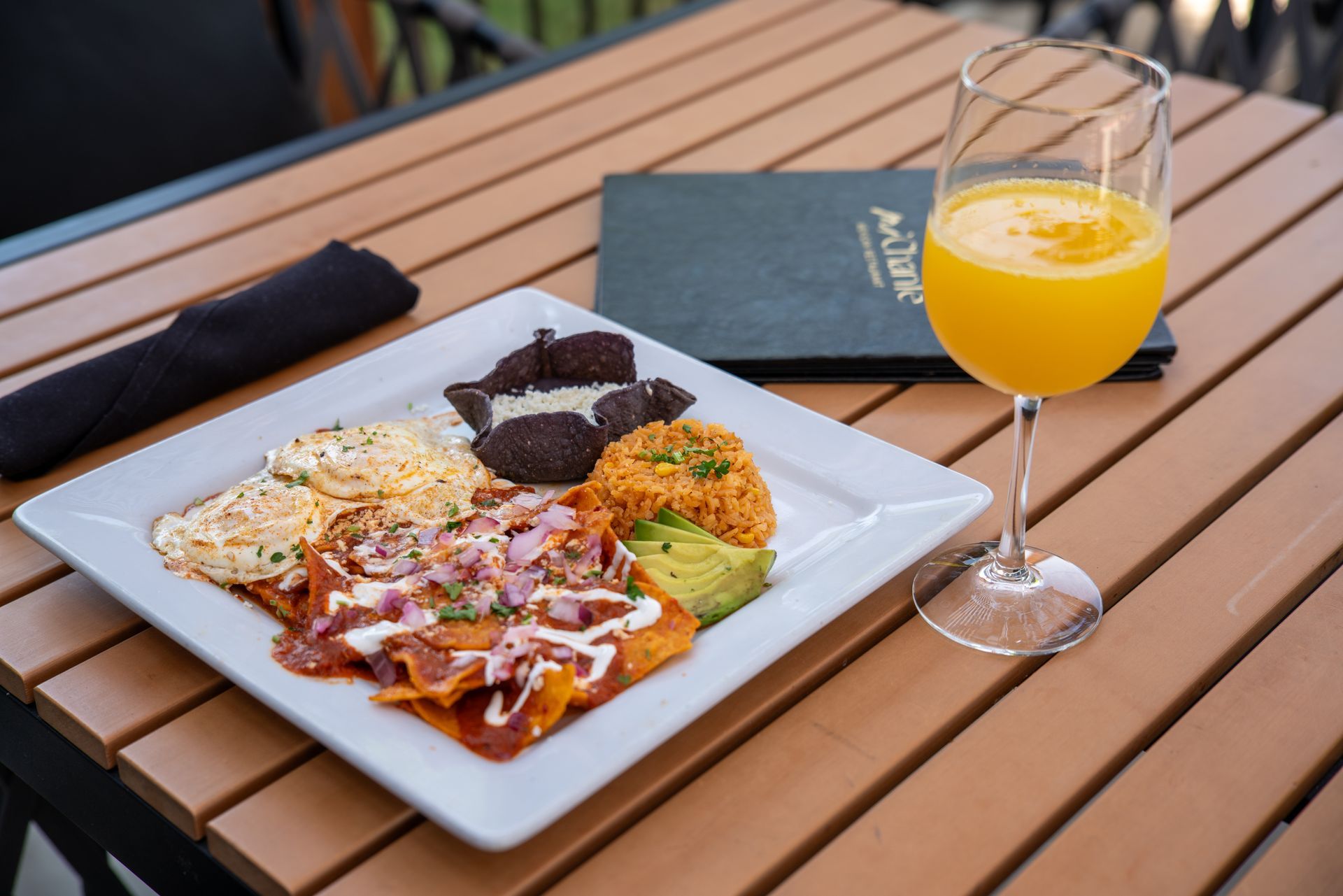 Square plate with chilaquiles, rice, avocado, and drink on a wooden table.