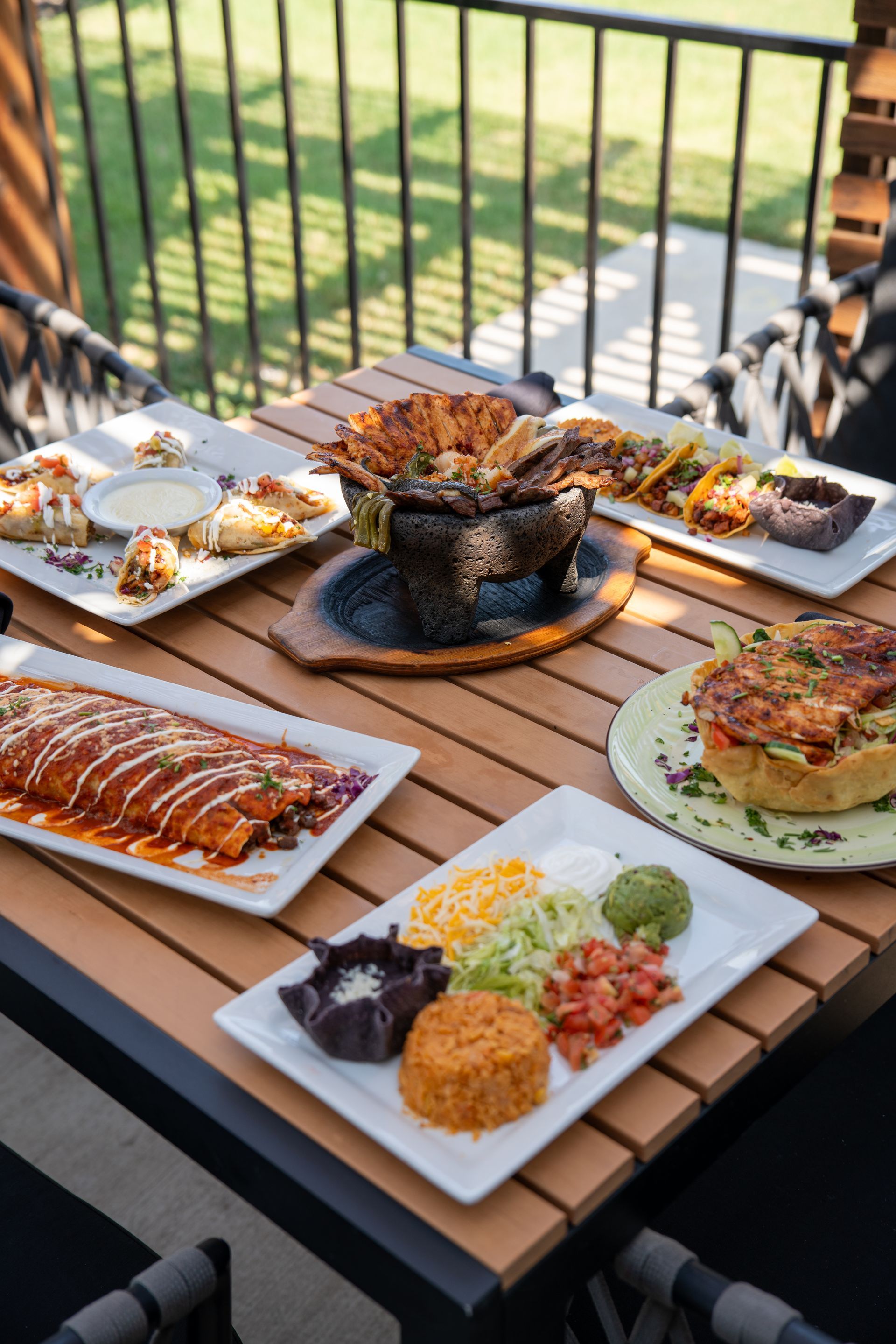 Mexican dishes on a wooden table outdoors. Enchiladas, tacos, rice, guacamole, and more.