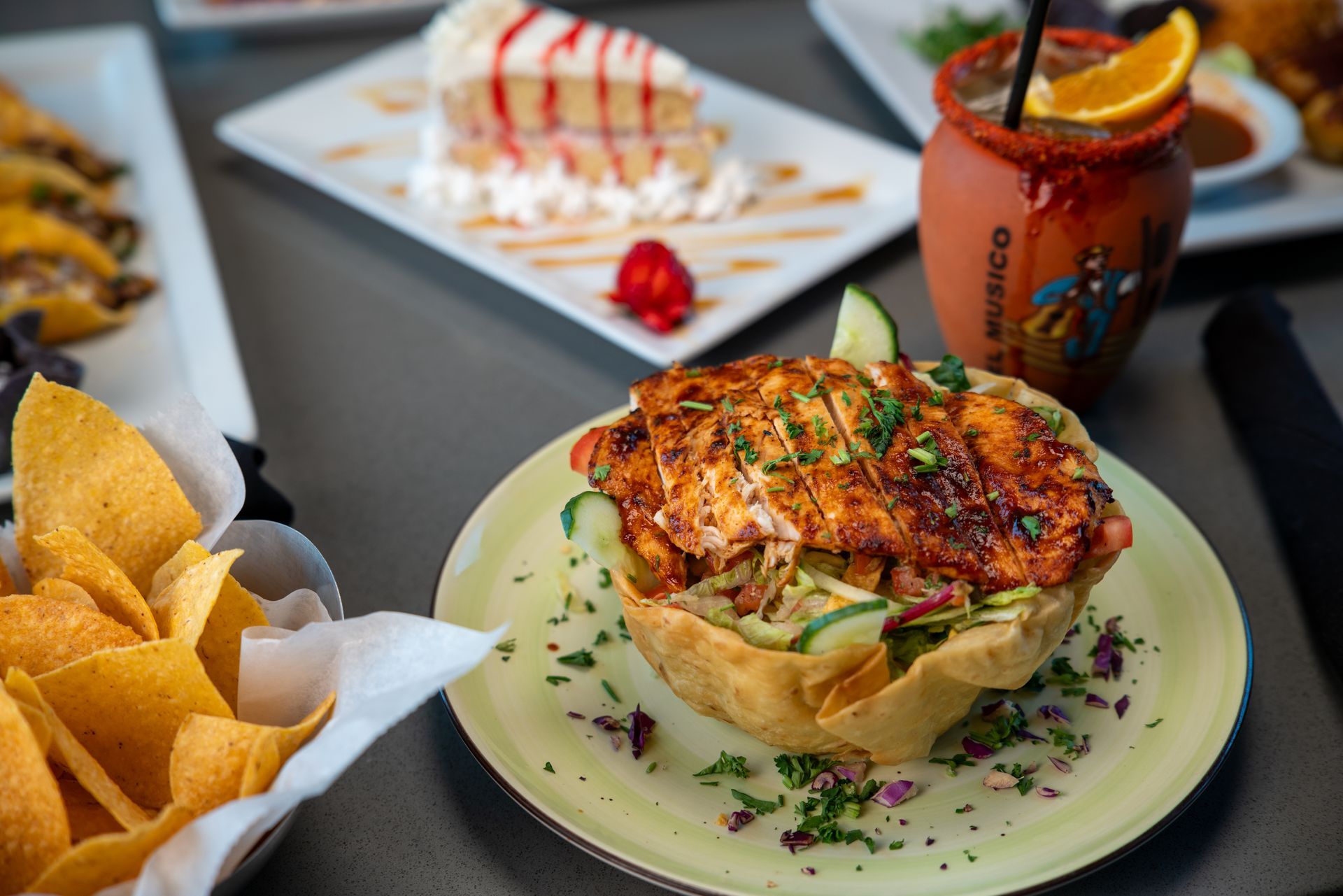 Mexican food spread: chicken salad in a tortilla bowl, chips, cake, cocktail.