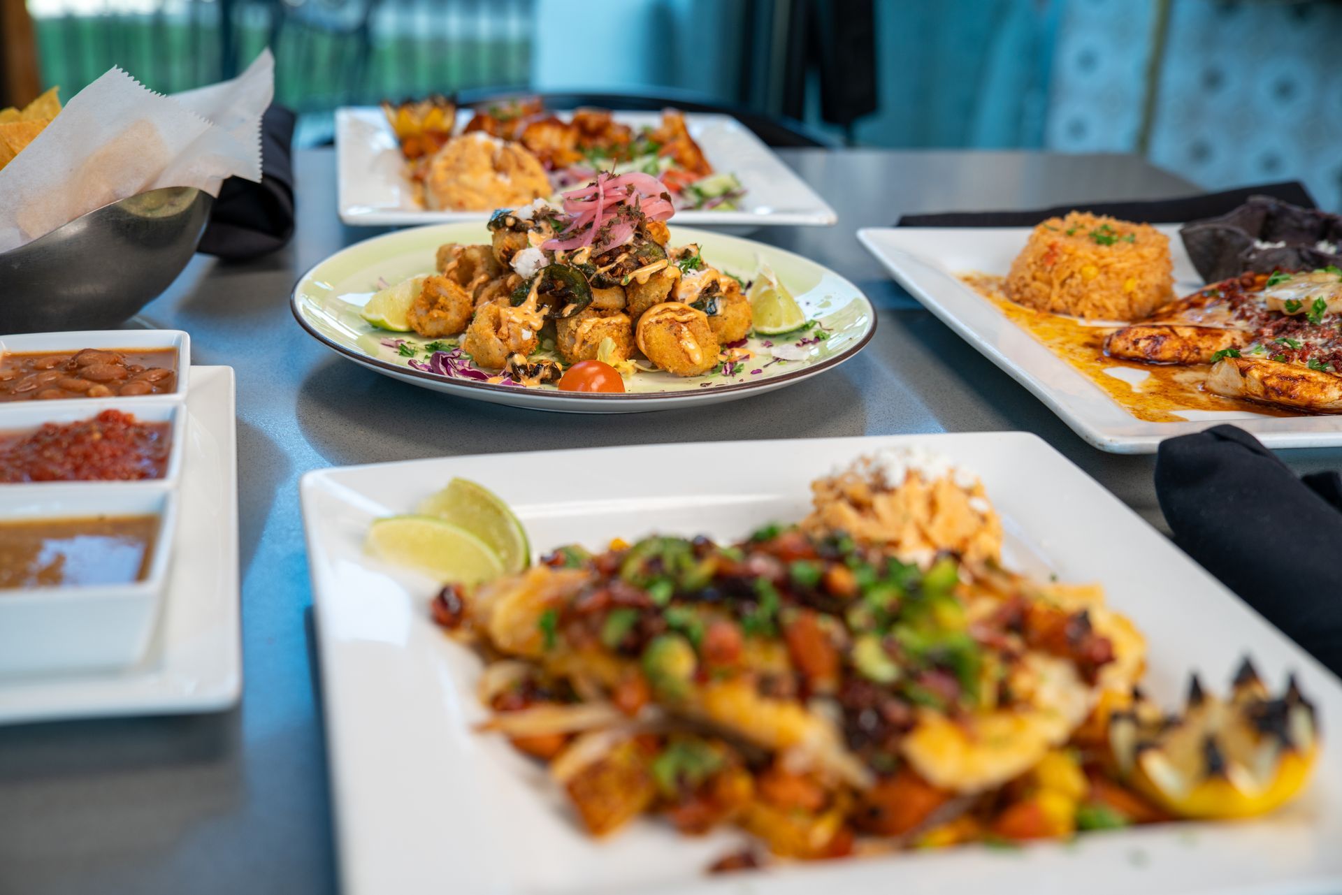 Several plates of Mexican food on a table, including fried dishes and fish.