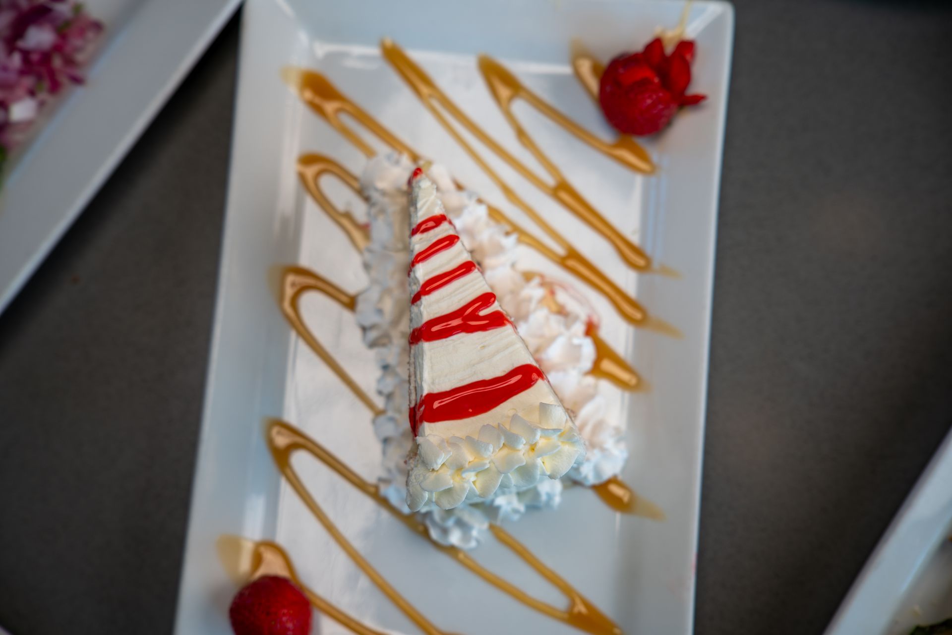 Slice of cake with whipped cream, caramel drizzle, and strawberries on a white plate.