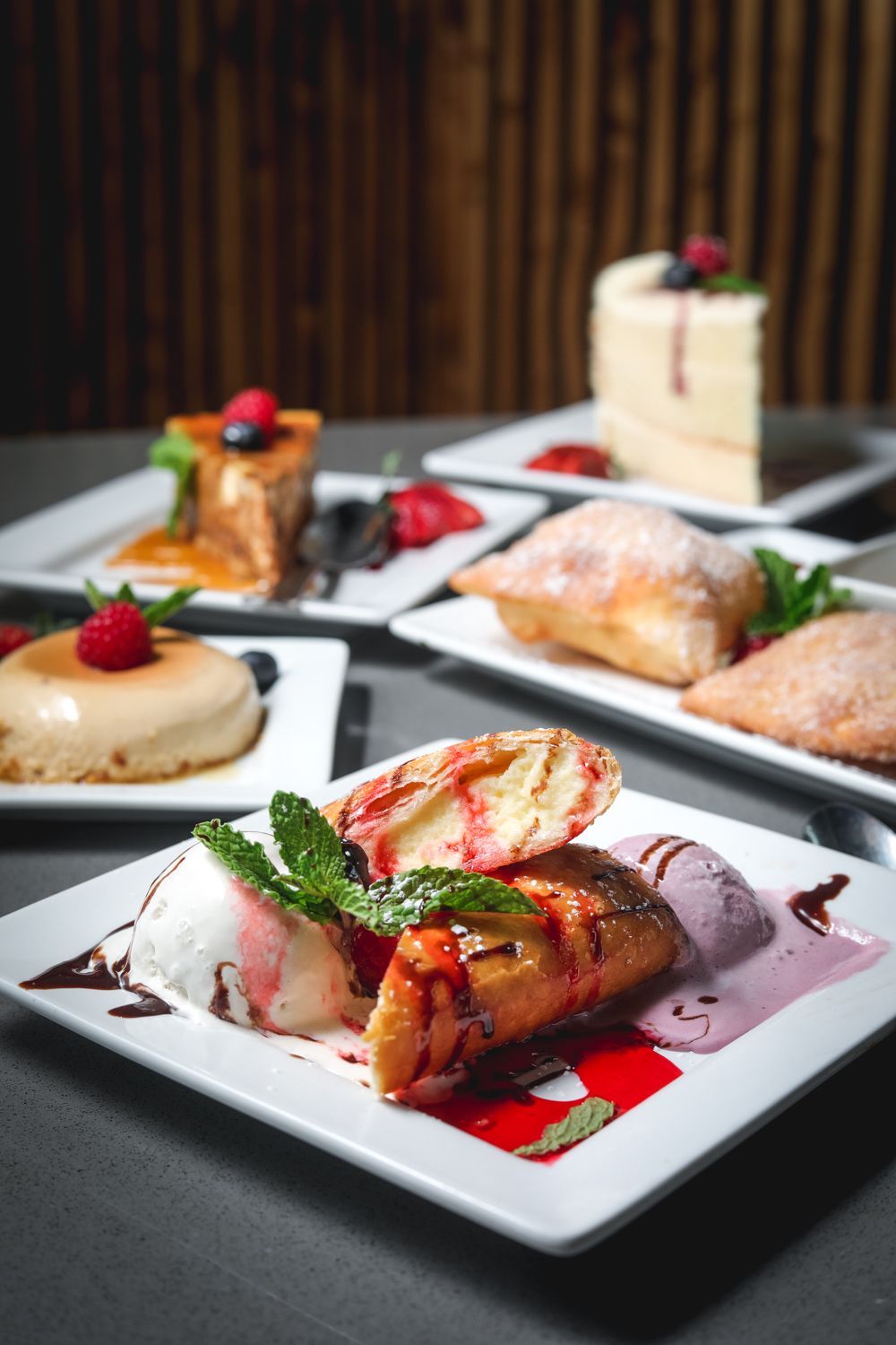Plates of desserts: cake, flan, fried pastries, and ice cream drizzled with sauce and berries.