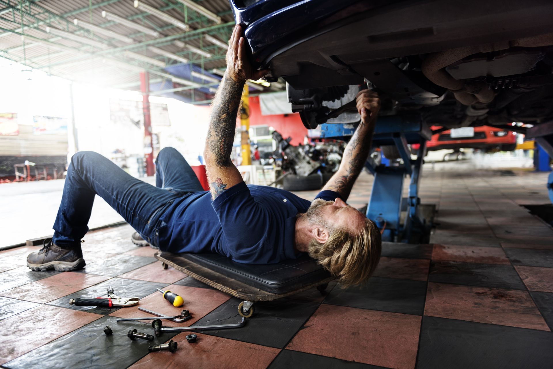 Mechanic working under a car on a creeper in a garage.