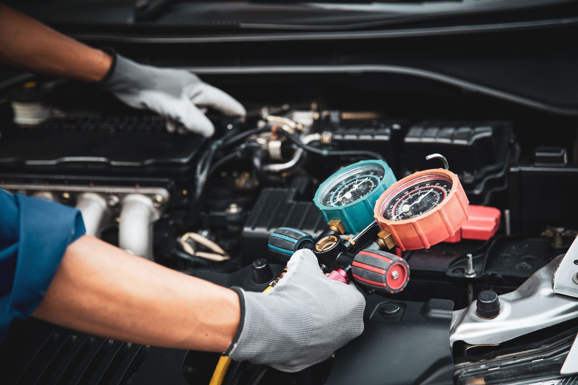Mechanic servicing car AC with gauges attached to engine components.