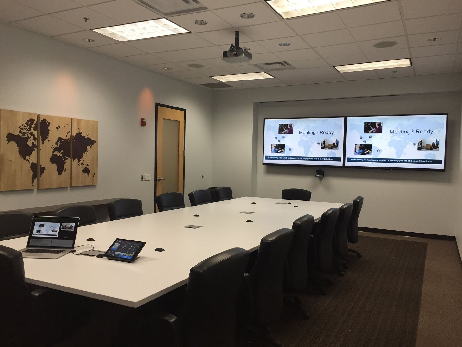 A conference room with a long table and chairs and two monitors on the wall.