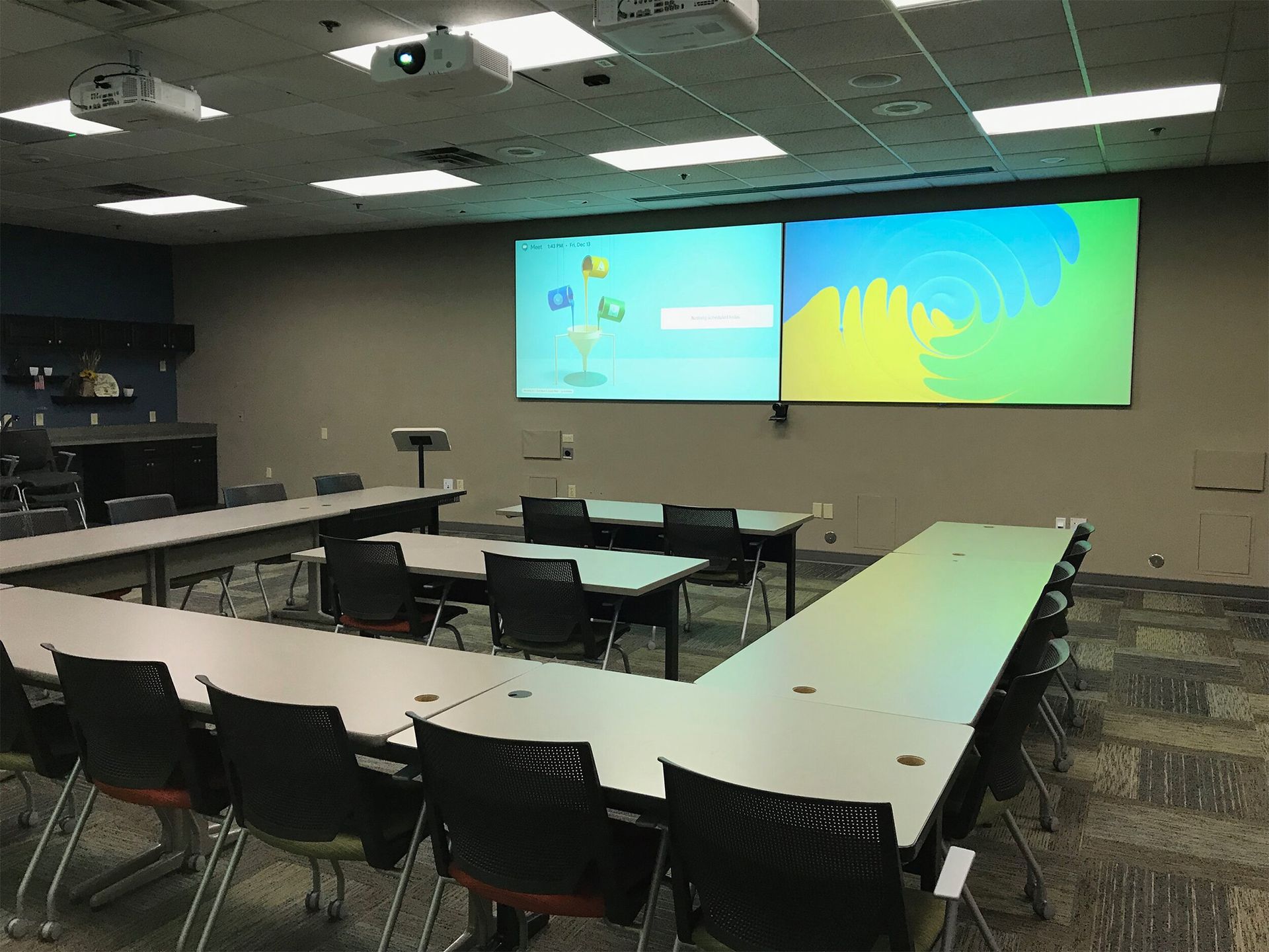 A classroom with tables and chairs and a large screen on the wall