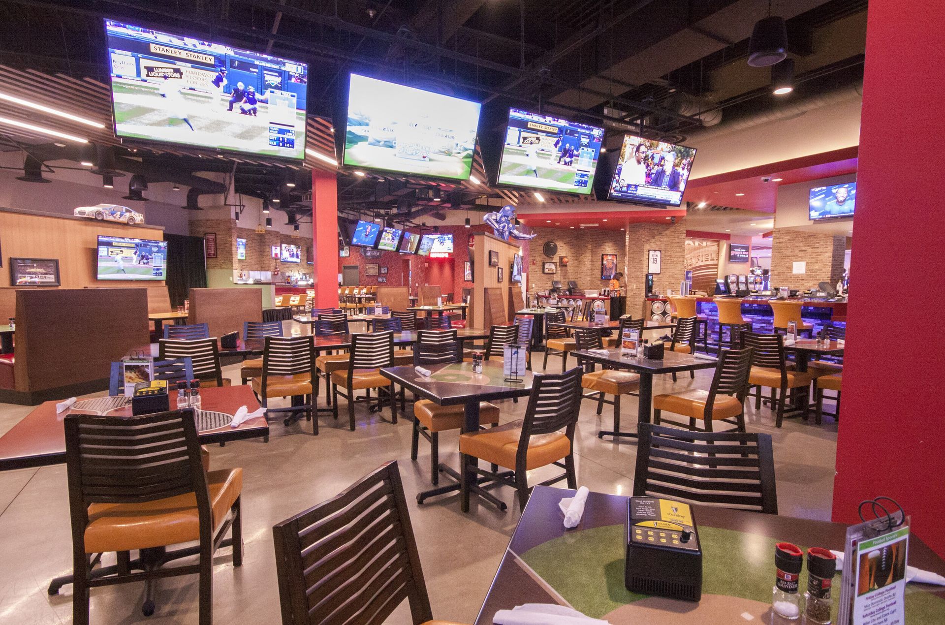 A restaurant with tables and chairs and televisions on the ceiling.