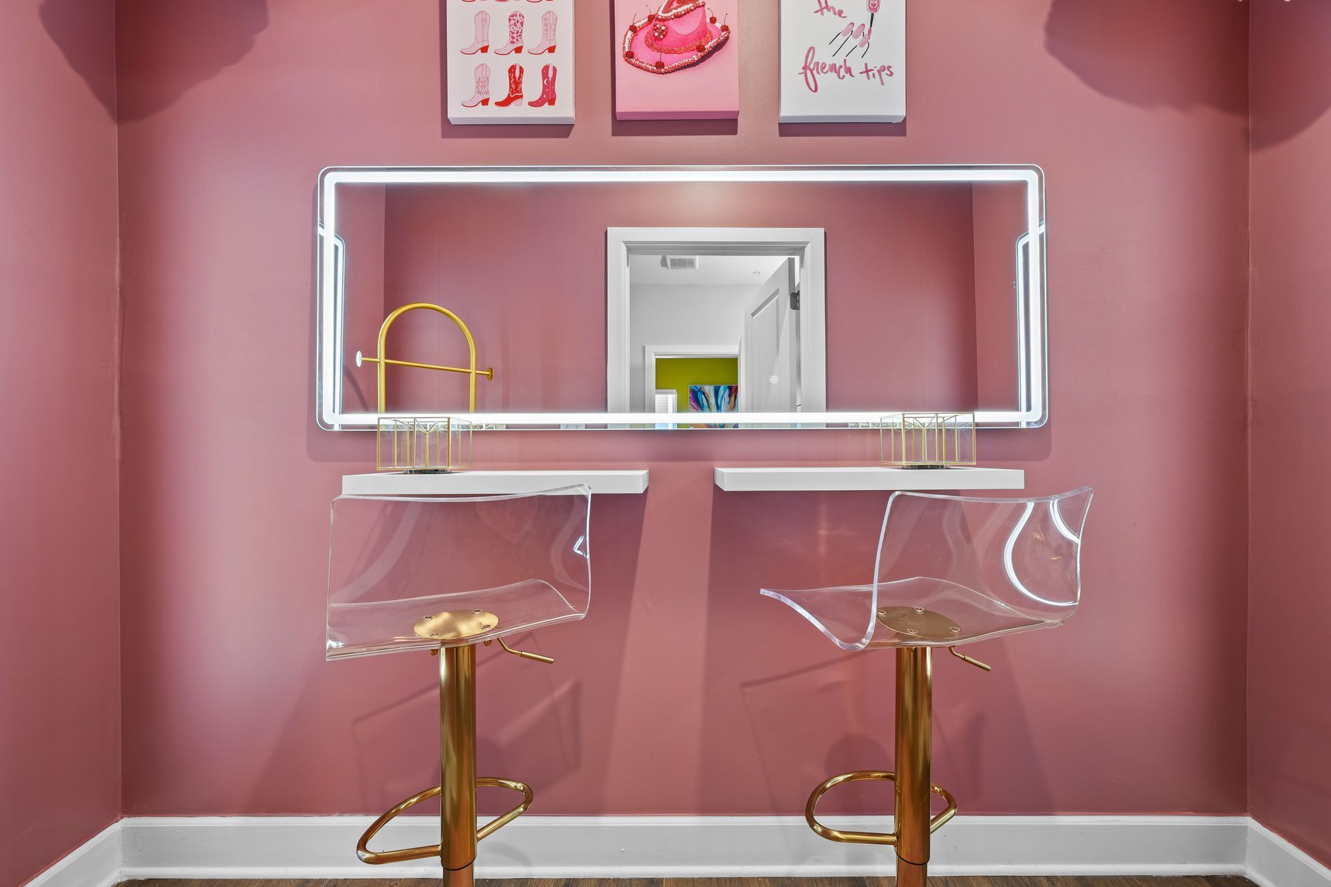 A pink room with two clear chairs and a mirror.