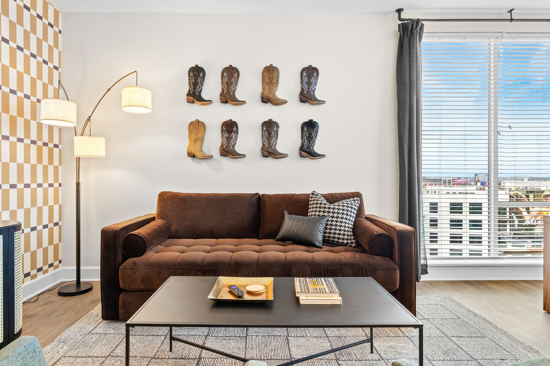 A living room with a brown couch , coffee table , and cowboy boots on the wall.