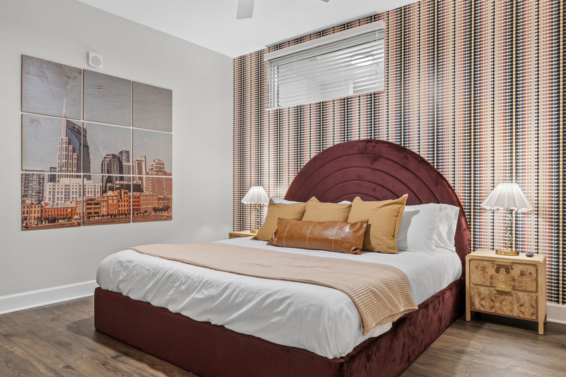 A bedroom with a large bed , nightstands , lamps and a painting on the wall.