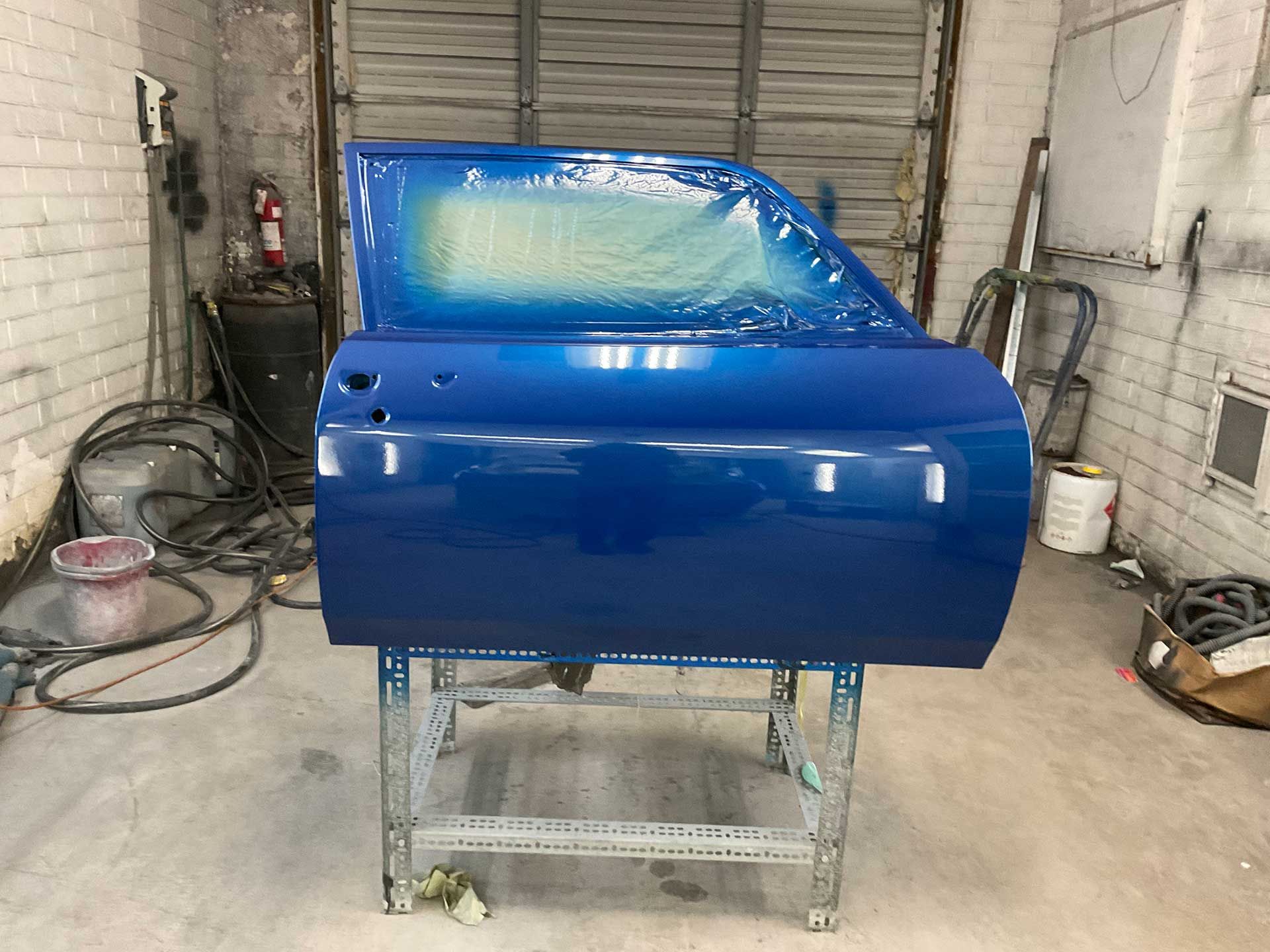 A blue car door is sitting on a stand in a garage