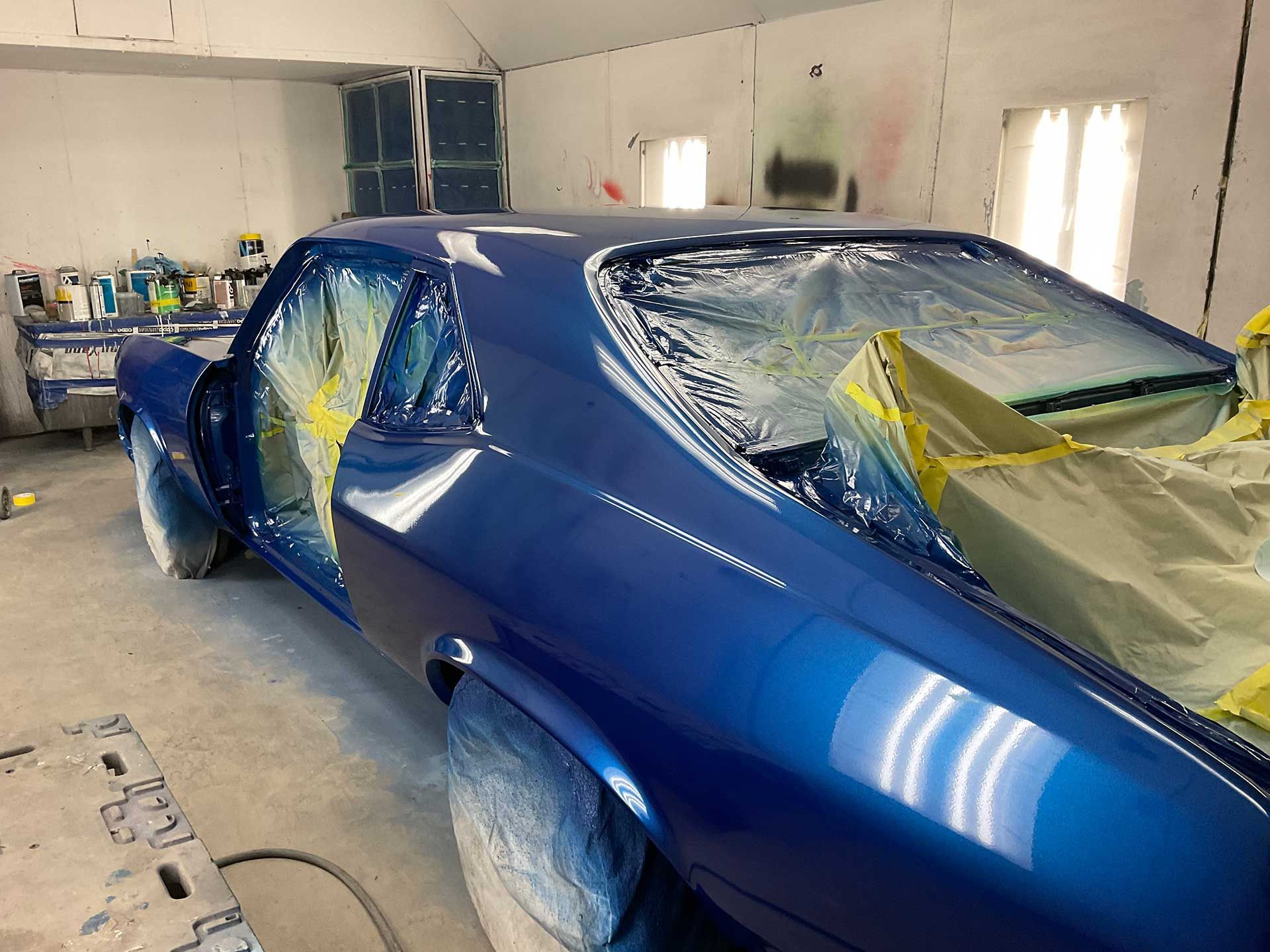 A blue car is being painted in a garage