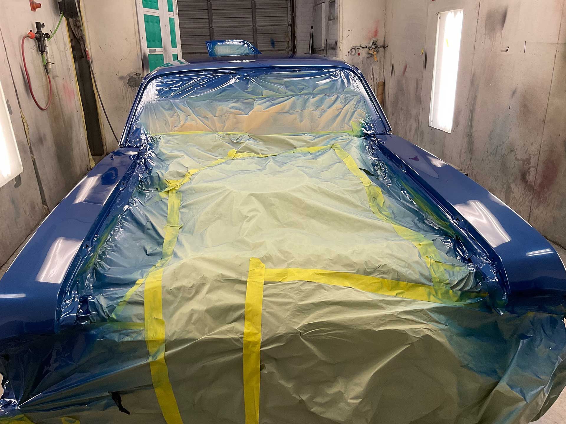 A blue car is being painted in a paint booth