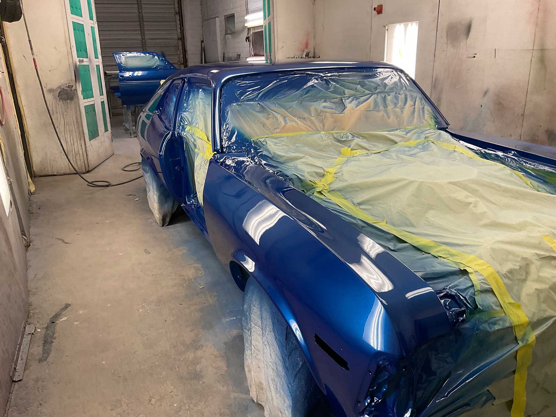 A shiny blue car is being painted in a garage